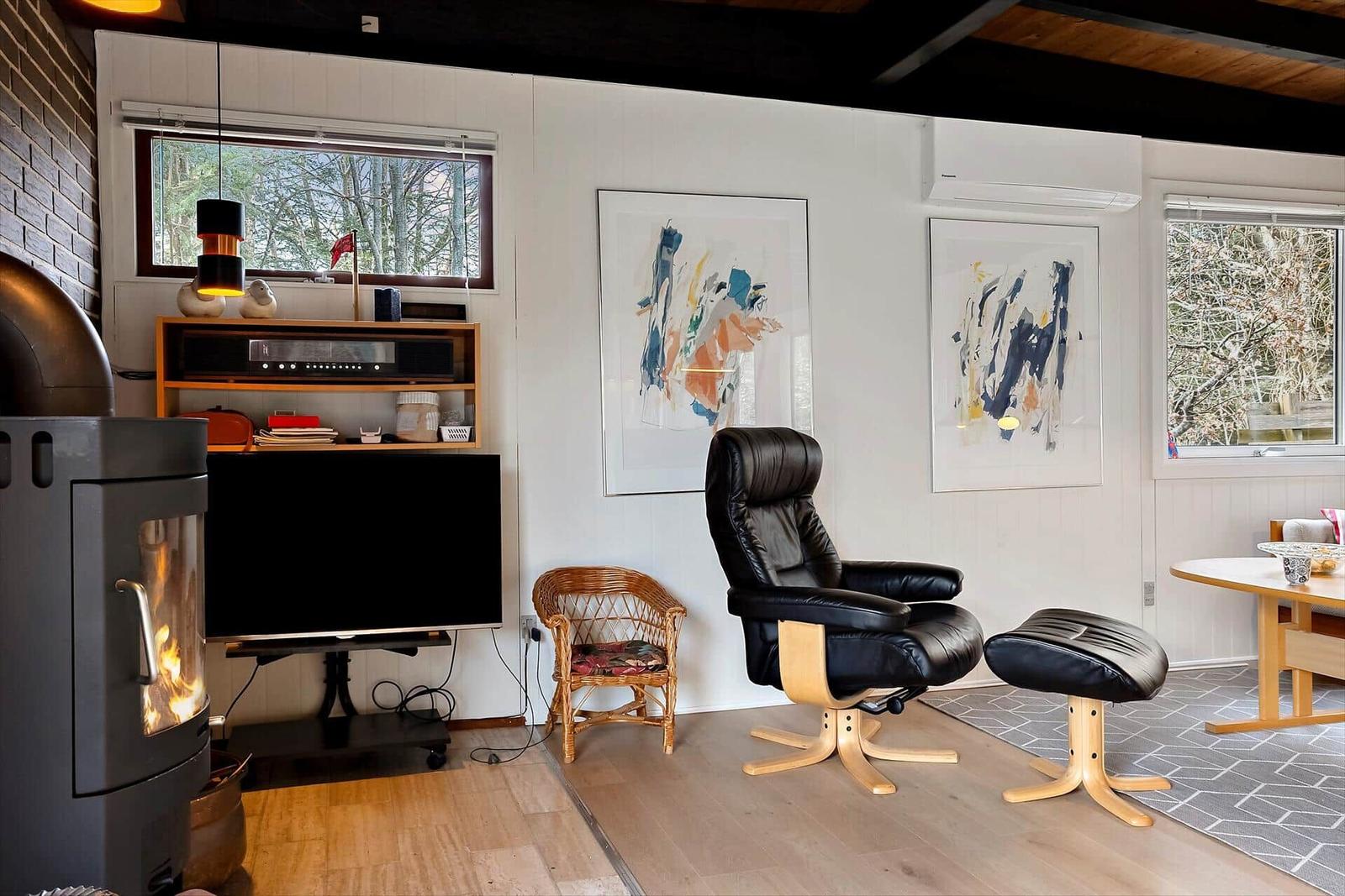 Wohnzimmer mit Kamin, TV, Sessel und Fenstern zum Wald