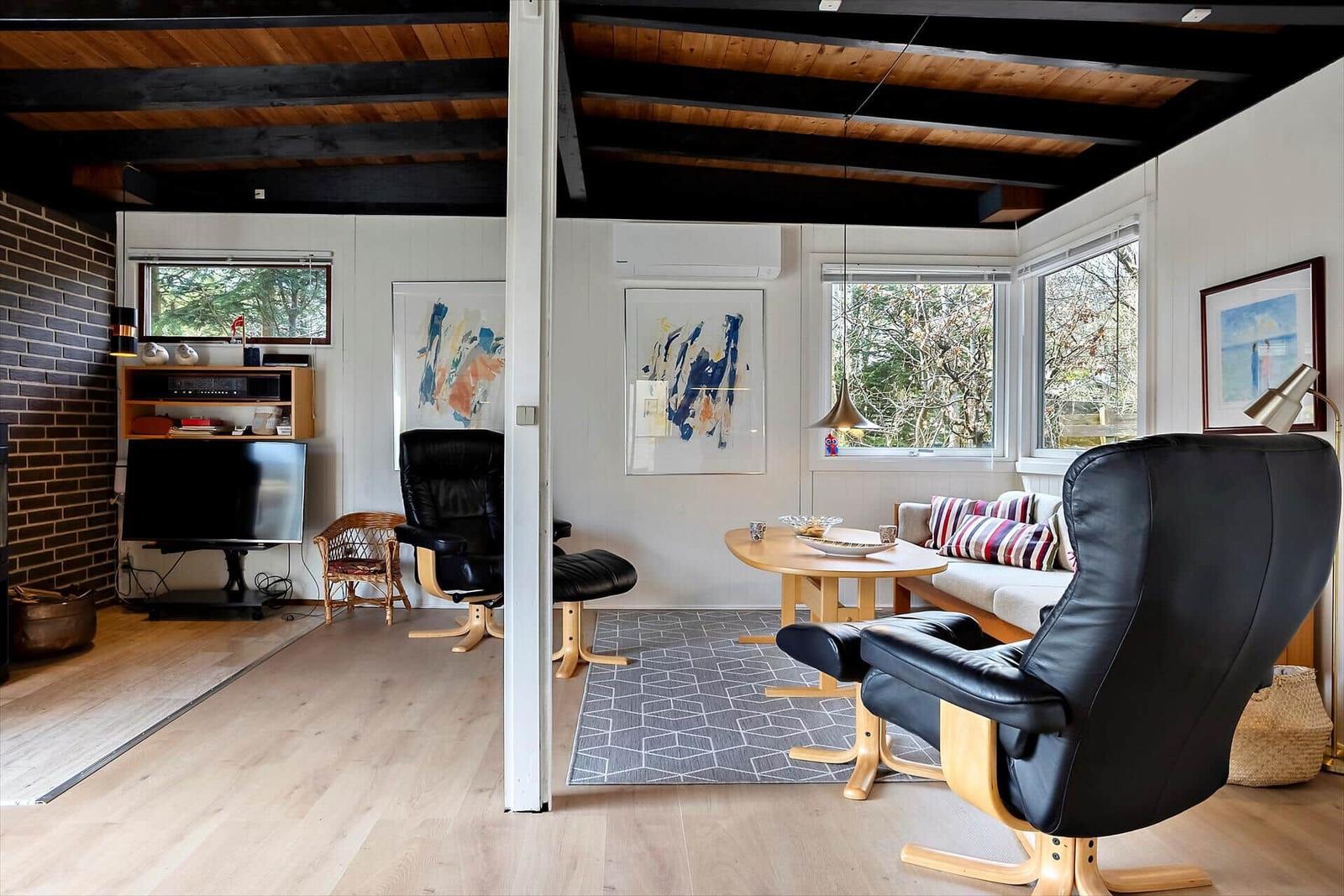 Wohnzimmer mit schwarzen Ledersesseln, Holztisch und Fenstern mit Blick auf Bäume.