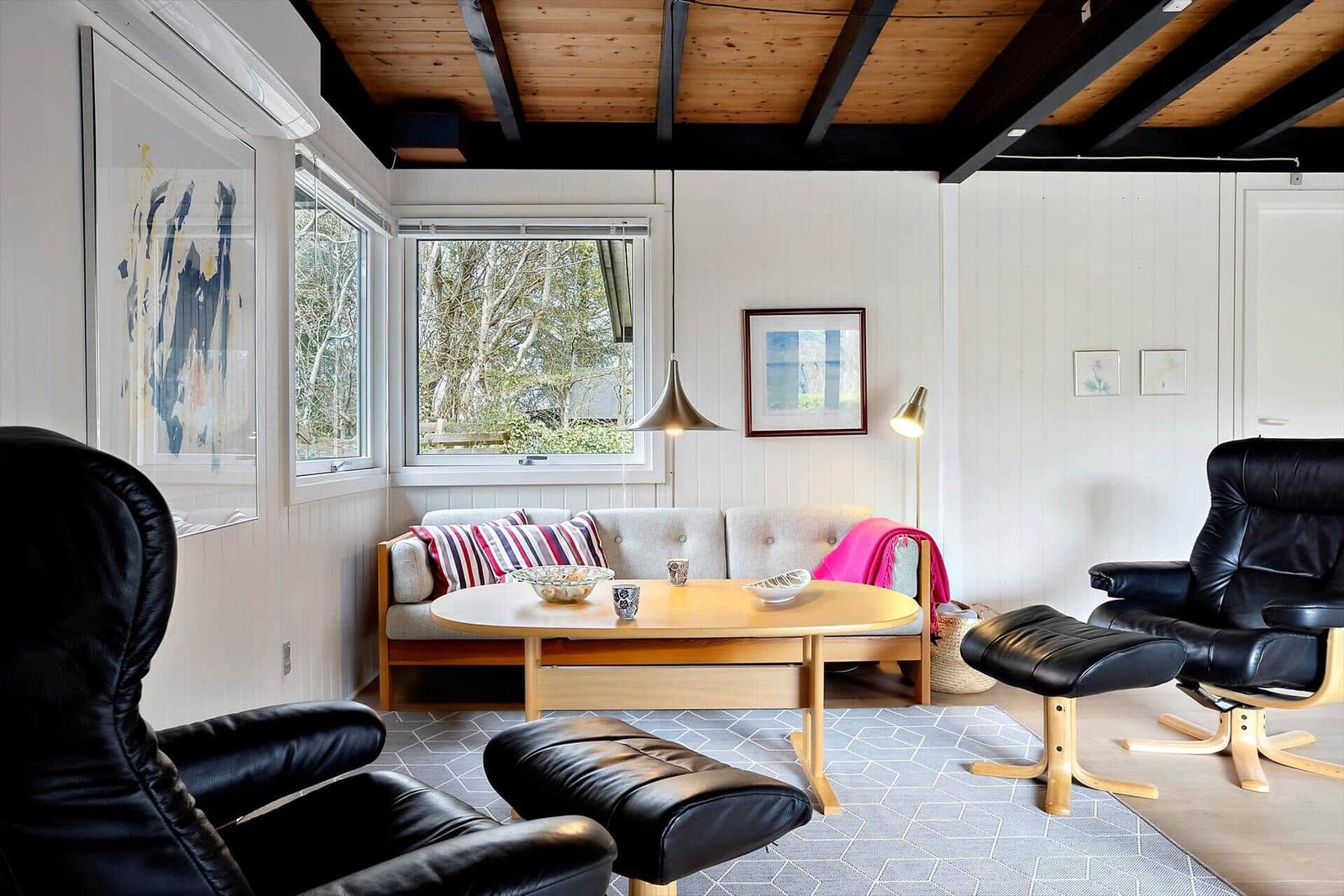 Wohnzimmer mit Sofa, zwei schwarzen Ledersessel und Holztisch unter Holzdecke.