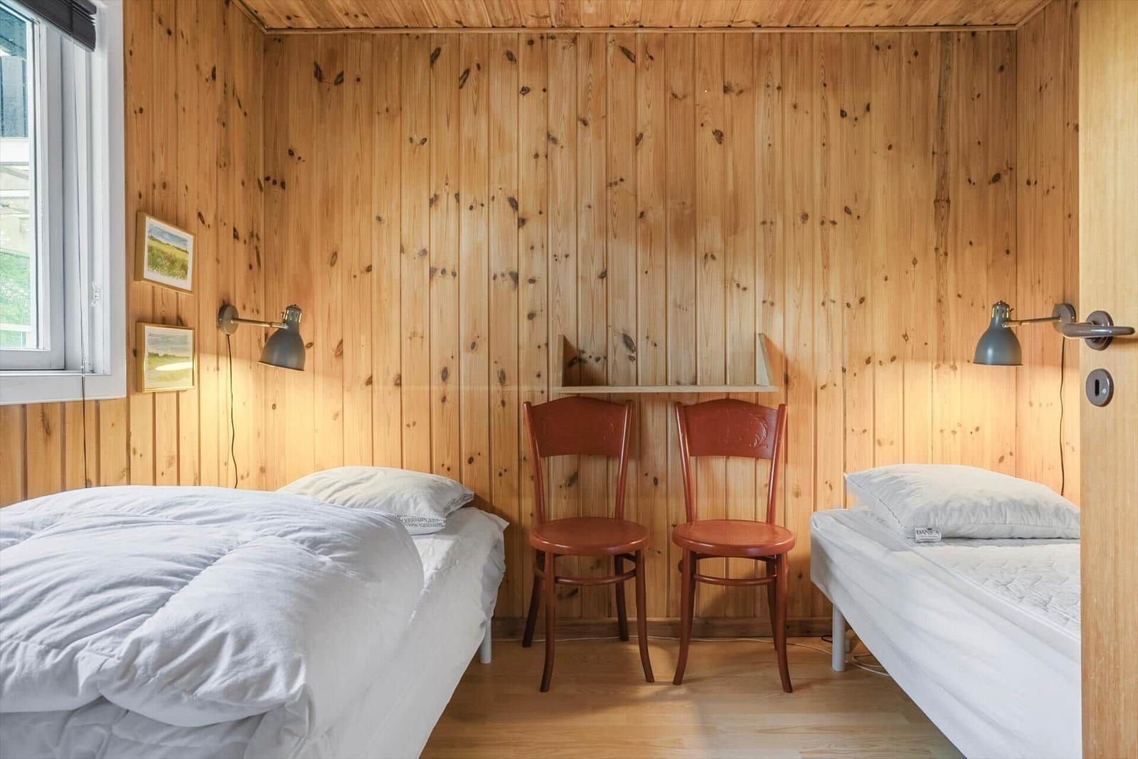 Zimmer mit zwei Betten, Holzwand und zwei Stühlen