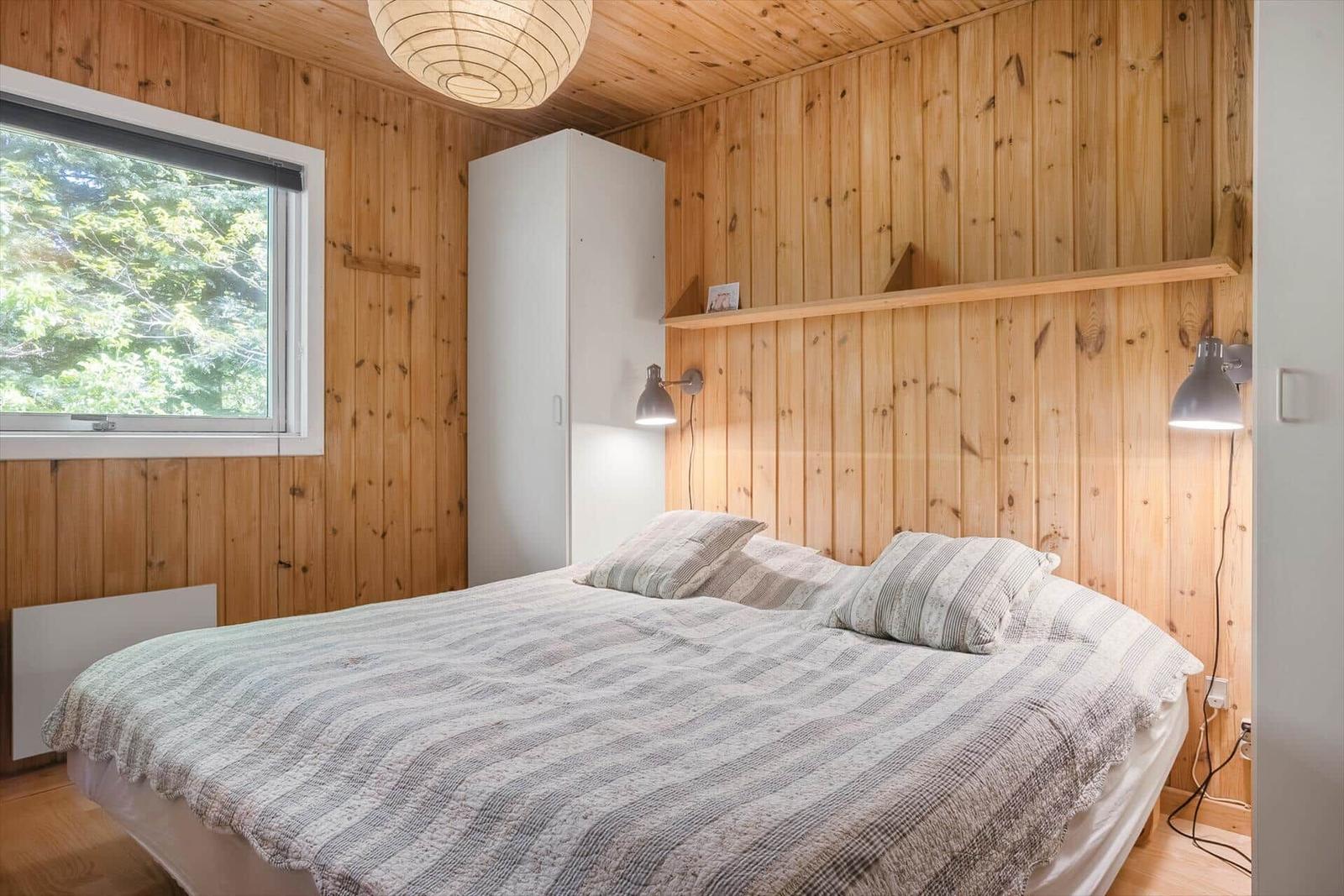 Schlafzimmer mit Holzwänden, Bett, Fenster und Schrank.