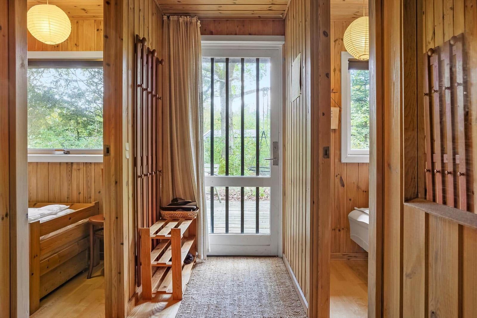 Hölzerner Flur mit Schlafzimmer und Bad. Tür führt auf Balkon mit Blick auf Wald.