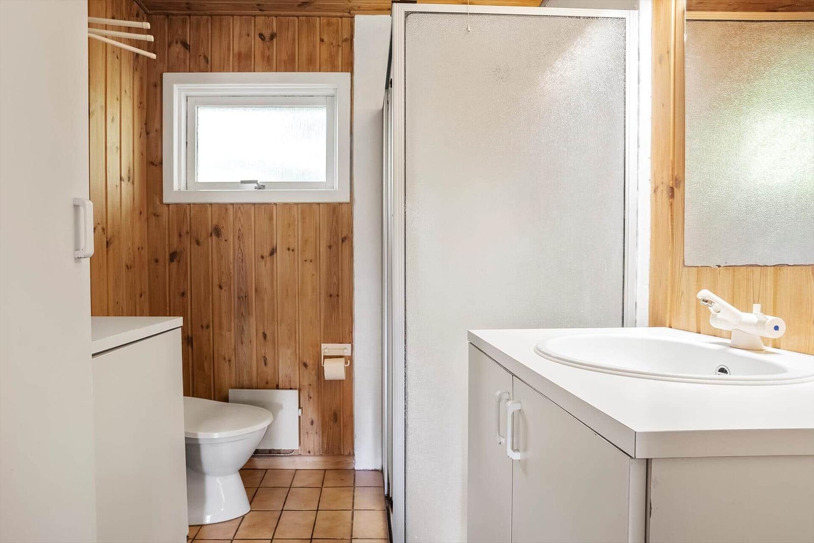 Badezimmer mit Toilette, Dusche und Waschbecken. Holzwände und Fliesenboden.