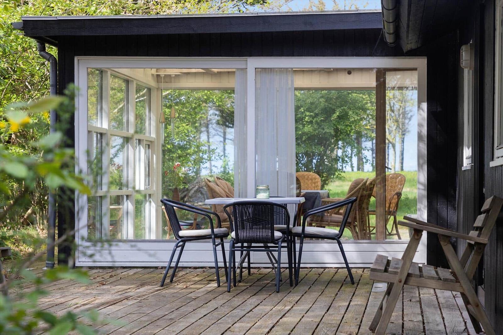 Terrasse mit Tisch und Stühlen vor einem Haus mit großem Fenster.