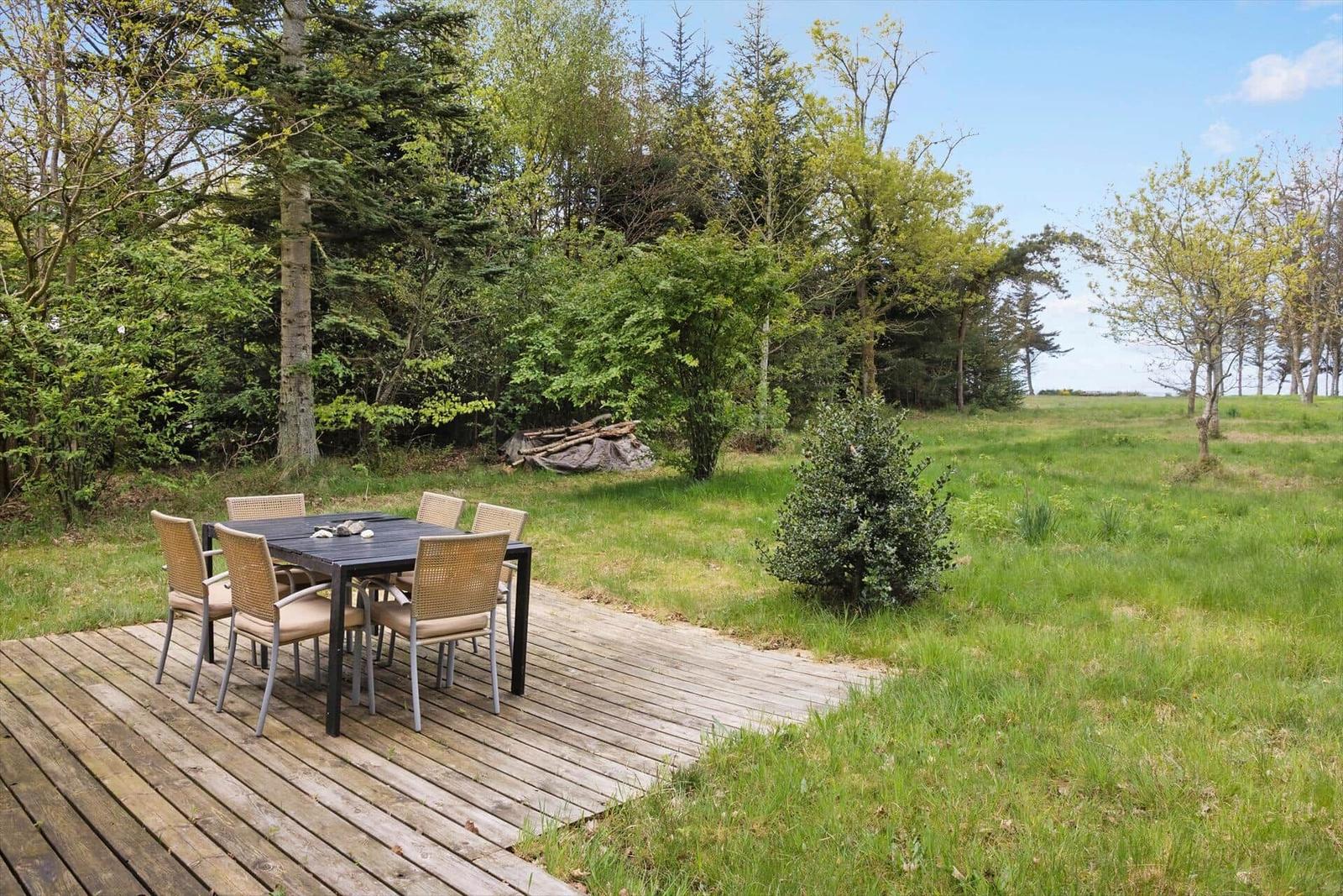 Holzterrasse mit Tisch und Stühlen im Grünen.
