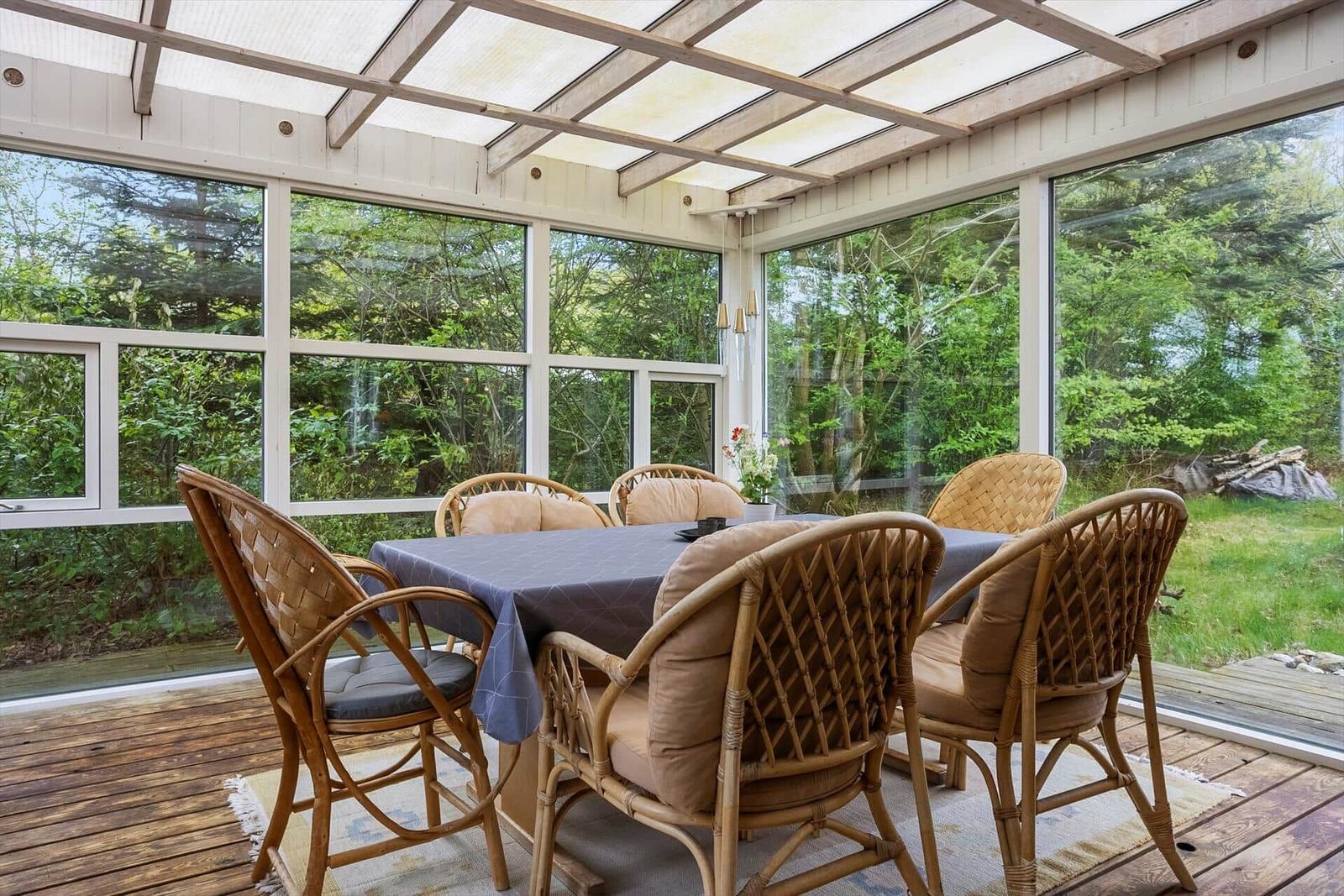 Draußenbereich mit Esstisch und Stühlen, großflächige Fenster, Blick auf grüne Umgebung.
