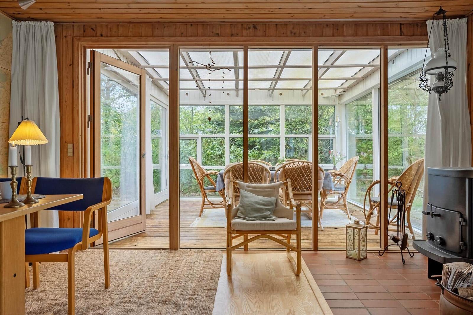 Haus mit Holzdecke, Glasfront und Terrasse mit Sitzgelegenheiten.