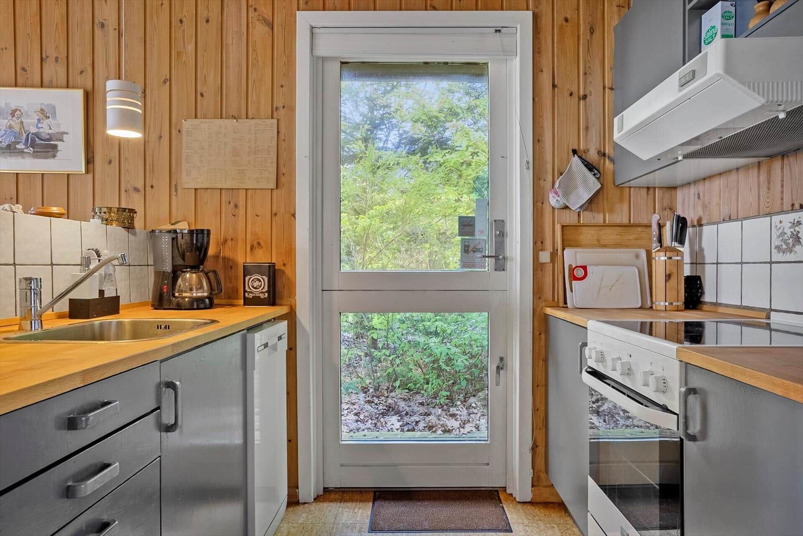 Küche mit Holzwand, Fenster zur Natur und Küchengeräten.