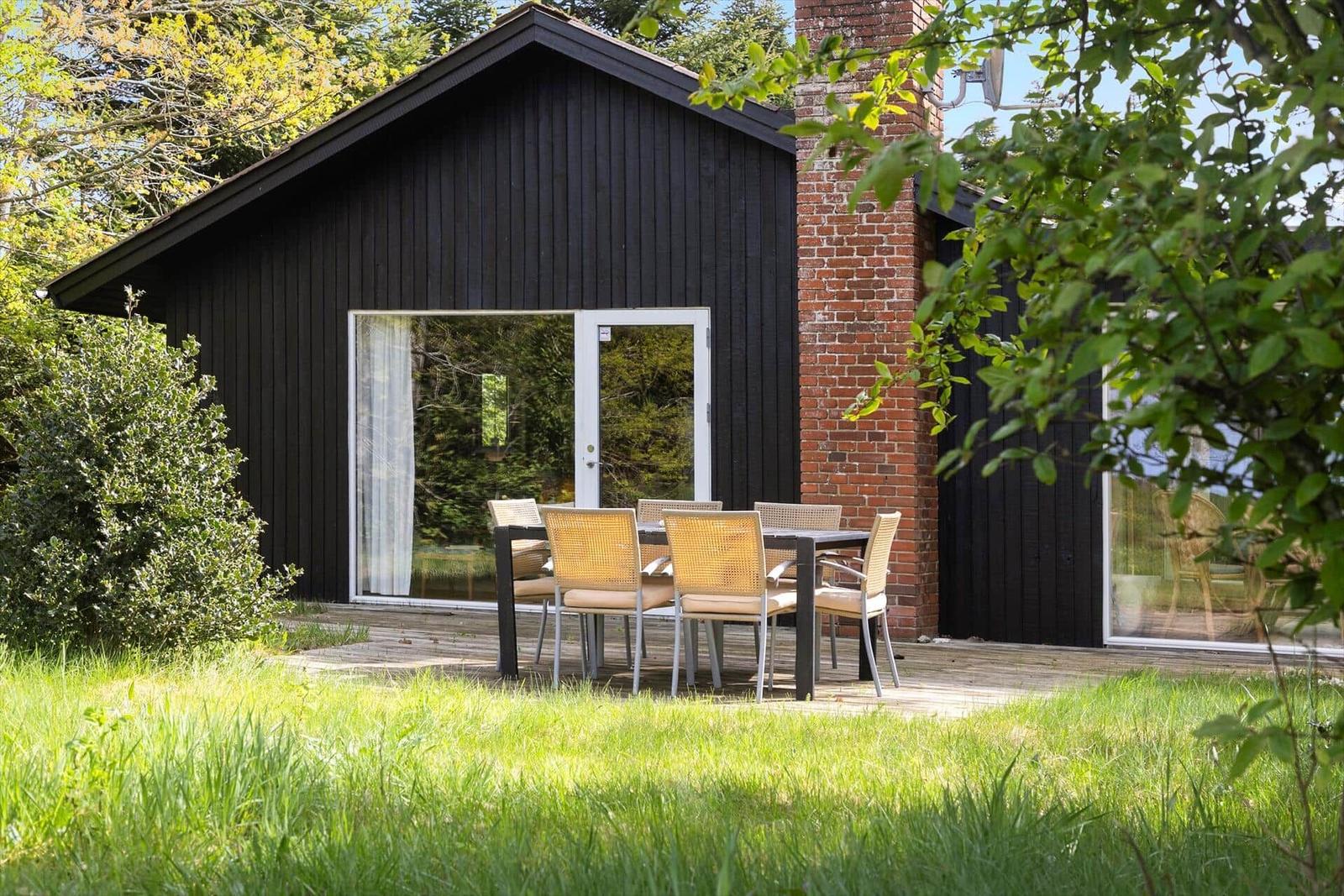 Schwarzes Holzhaus mit Terrasse und Sitzgruppe im Grünen