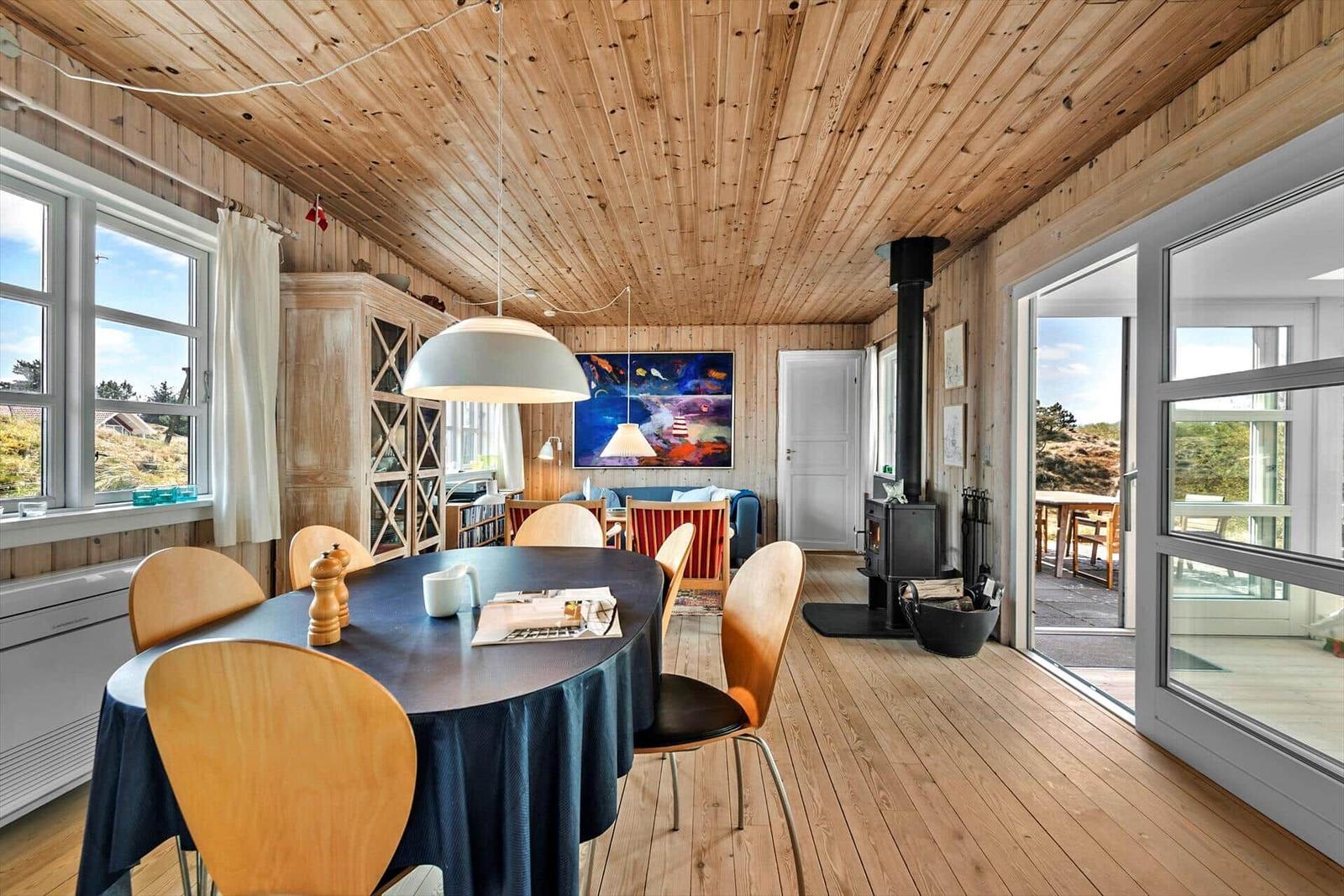 Essbereich mit Tisch und Stühlen, Holzdecke und -boden, Kamin und Fenster mit Blick nach draußen.