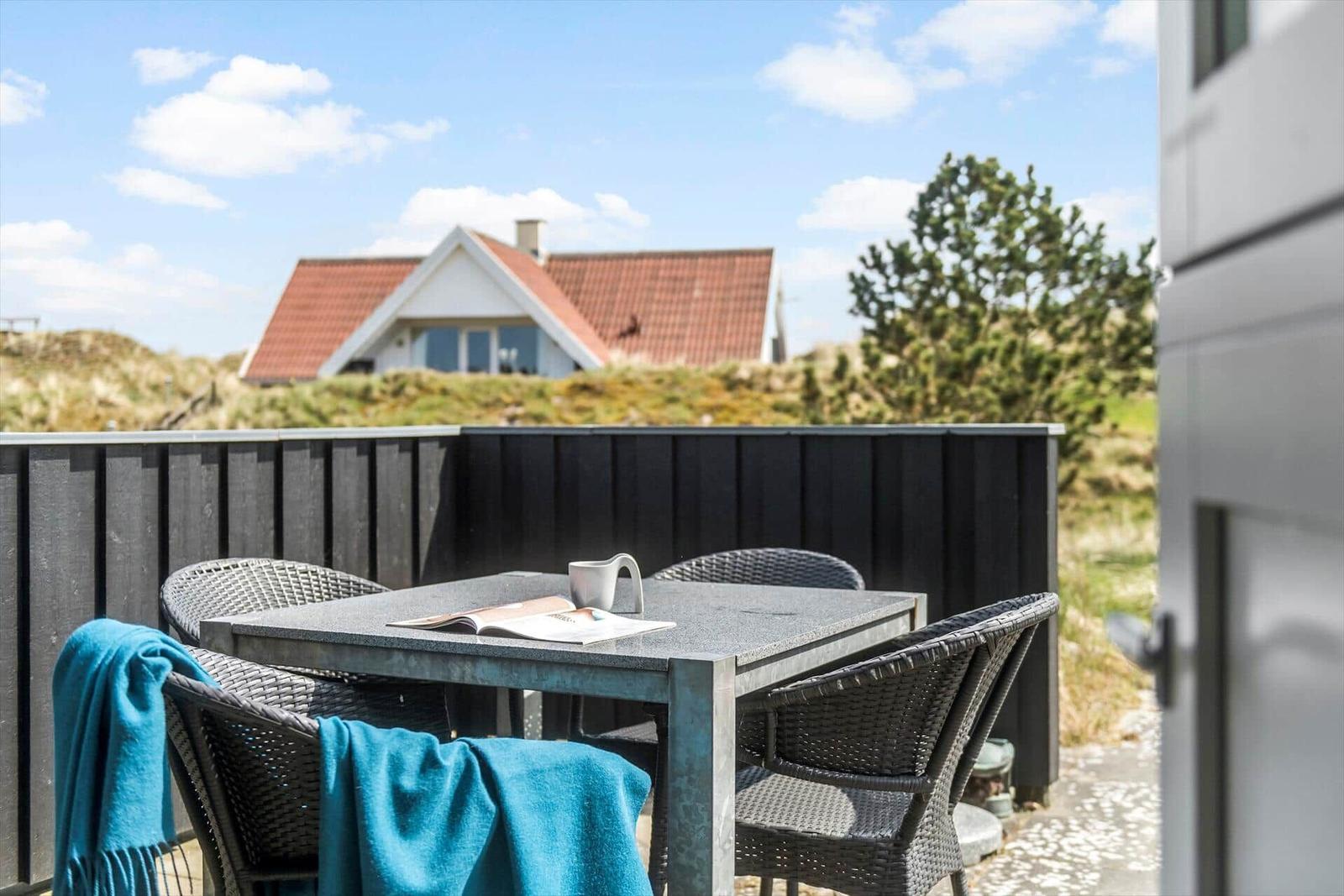 Terrasse mit Tisch und Stühlen. Im Hintergrund Haus und Grünflächen.