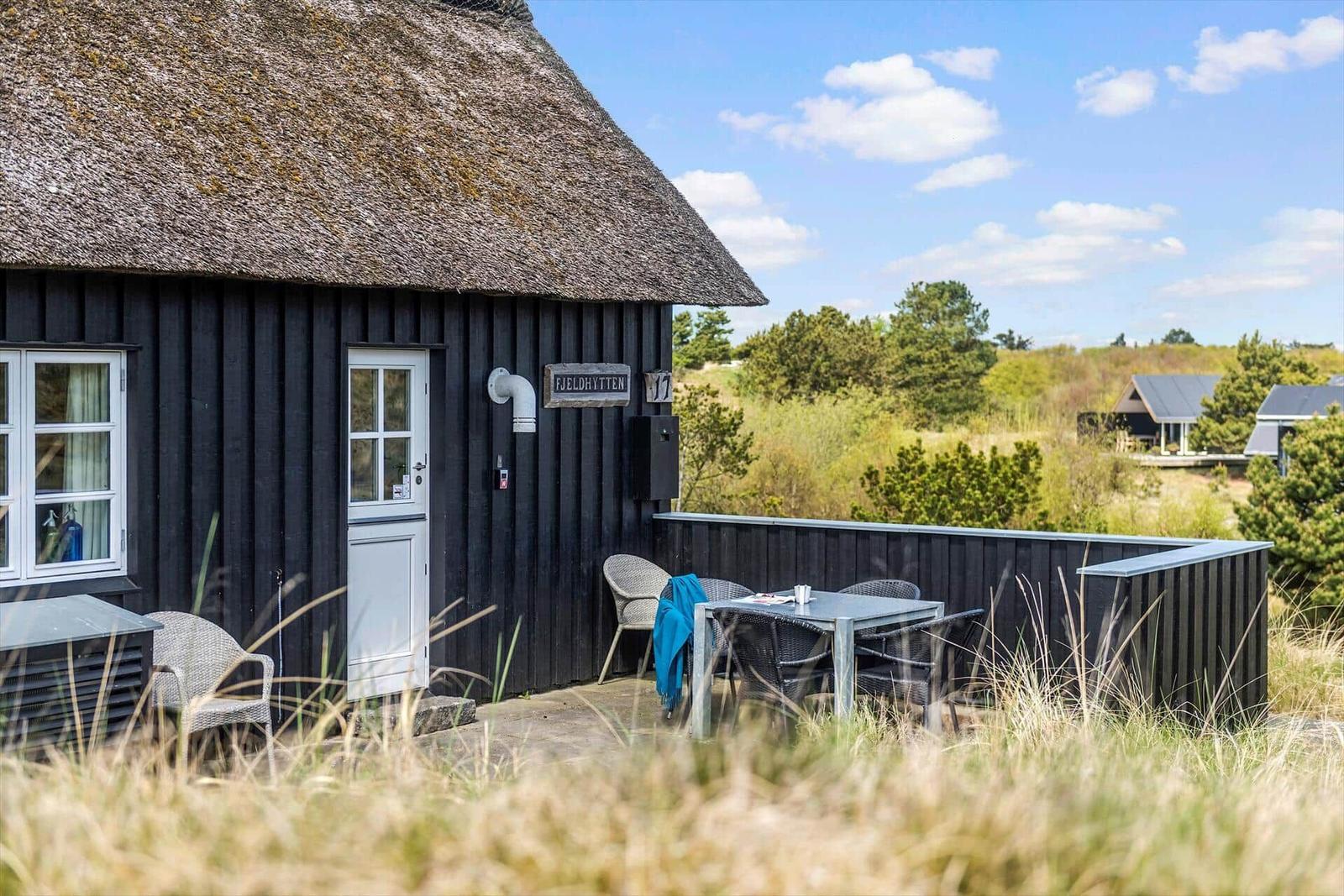 Schwarze Hütte mit Strohdach und Terrasse mit Tisch und Stühlen.