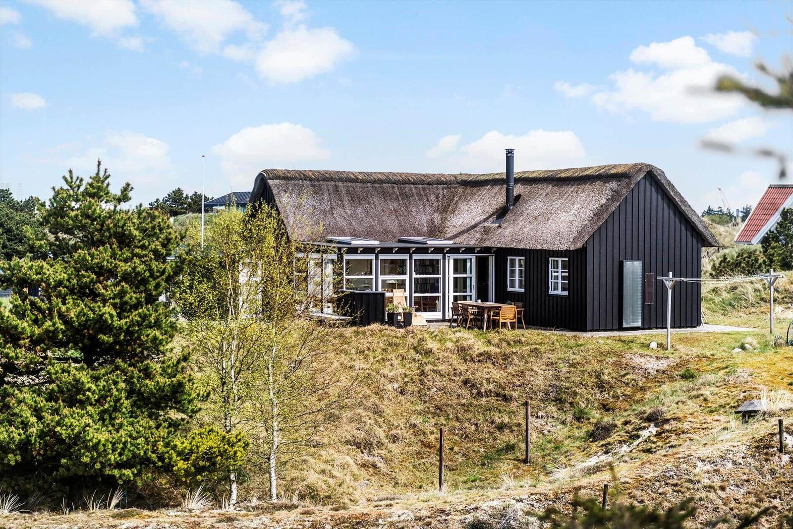 Schwarzes Haus mit Strohdach und großer Terrasse im Grünen.