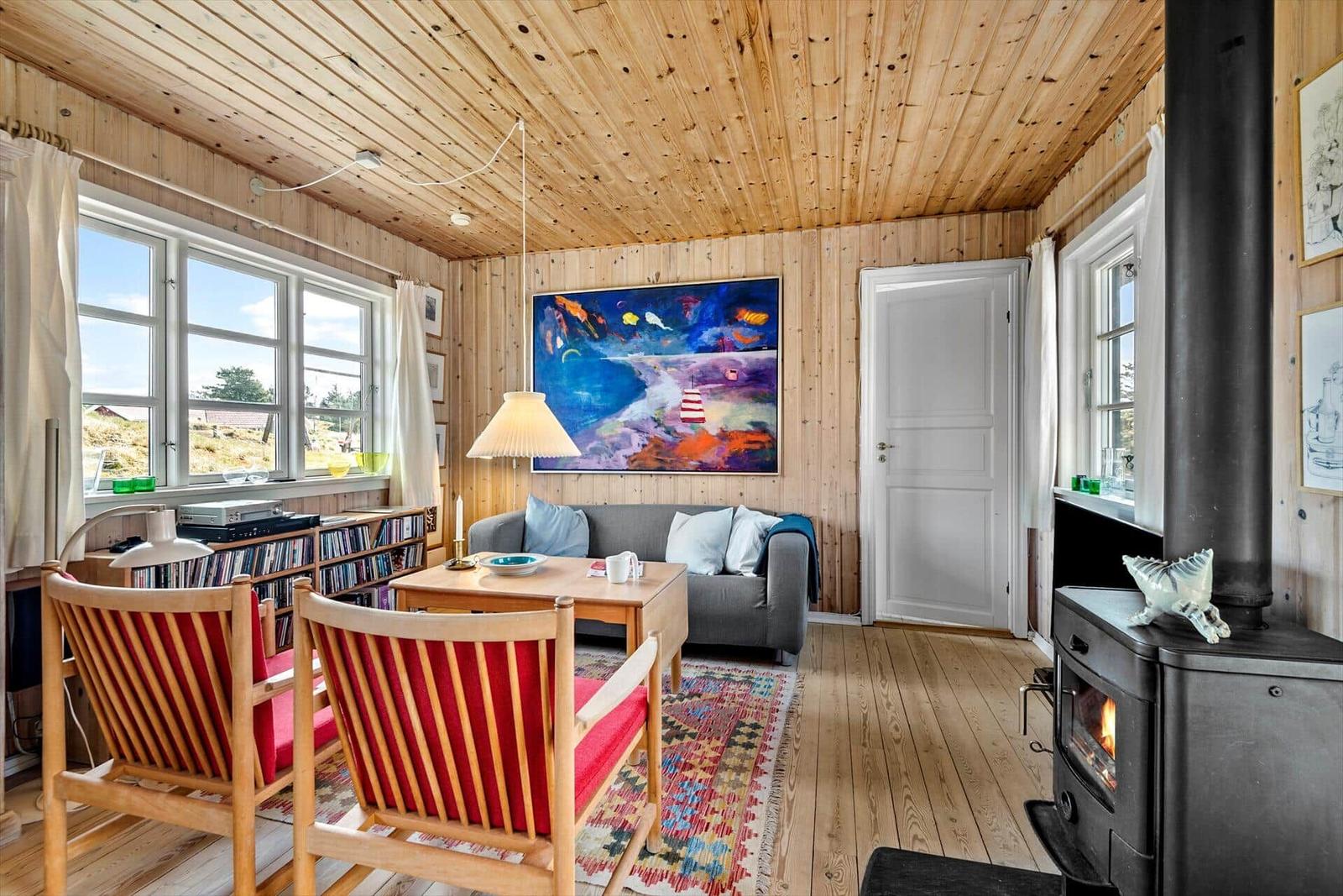 Wohnzimmer mit Holzwand, Kamin und großem Fenster. Sofa, Stühle und Wandbild sind sichtbar.