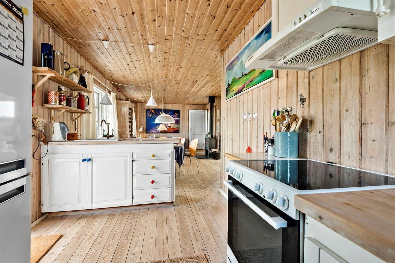 Küche mit Holzwänden und -boden, weißen Schränken und Edelstahlgeräten.