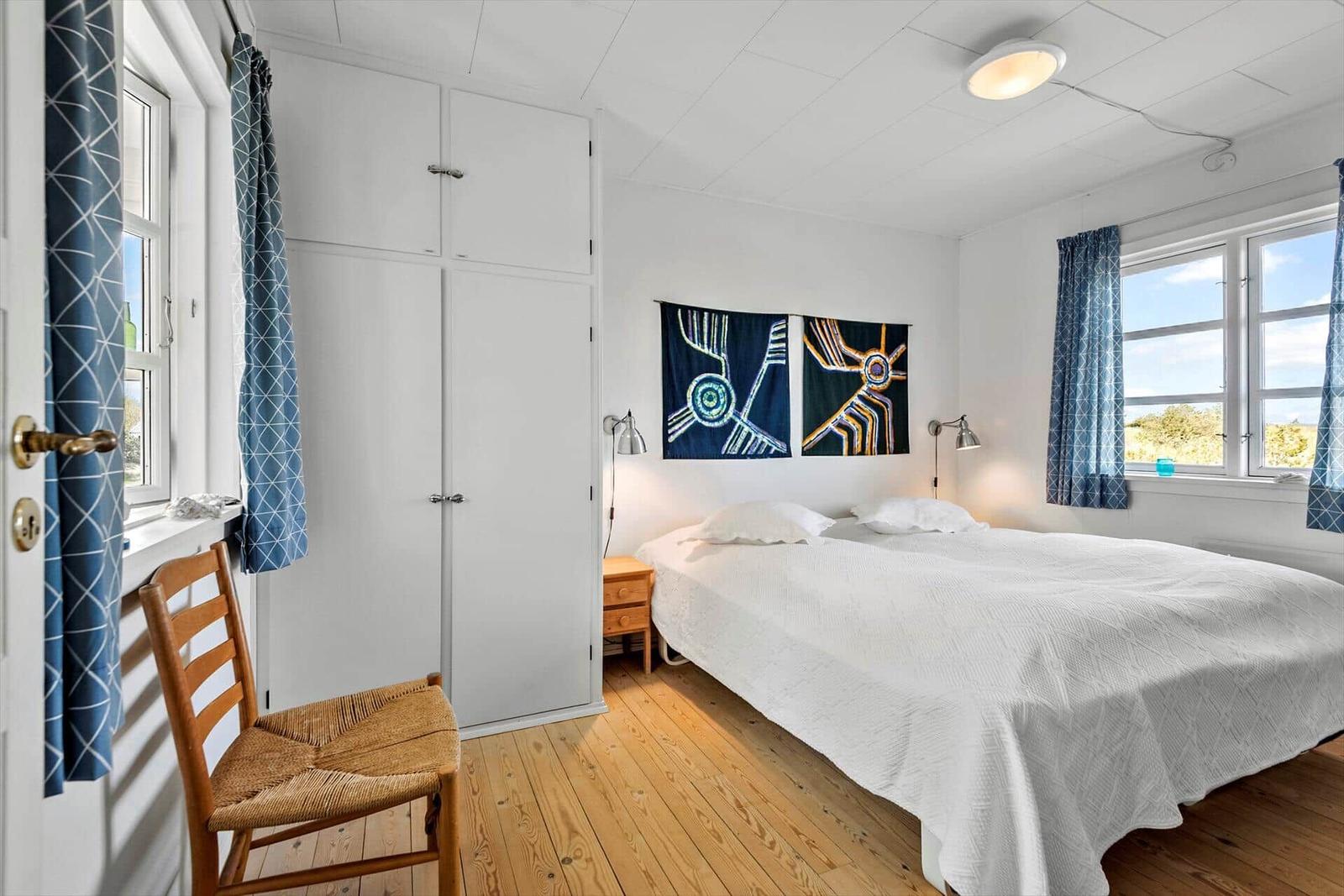 Schlafzimmer mit Bett, Kleiderschrank und Fenstern mit blauen Vorhängen.