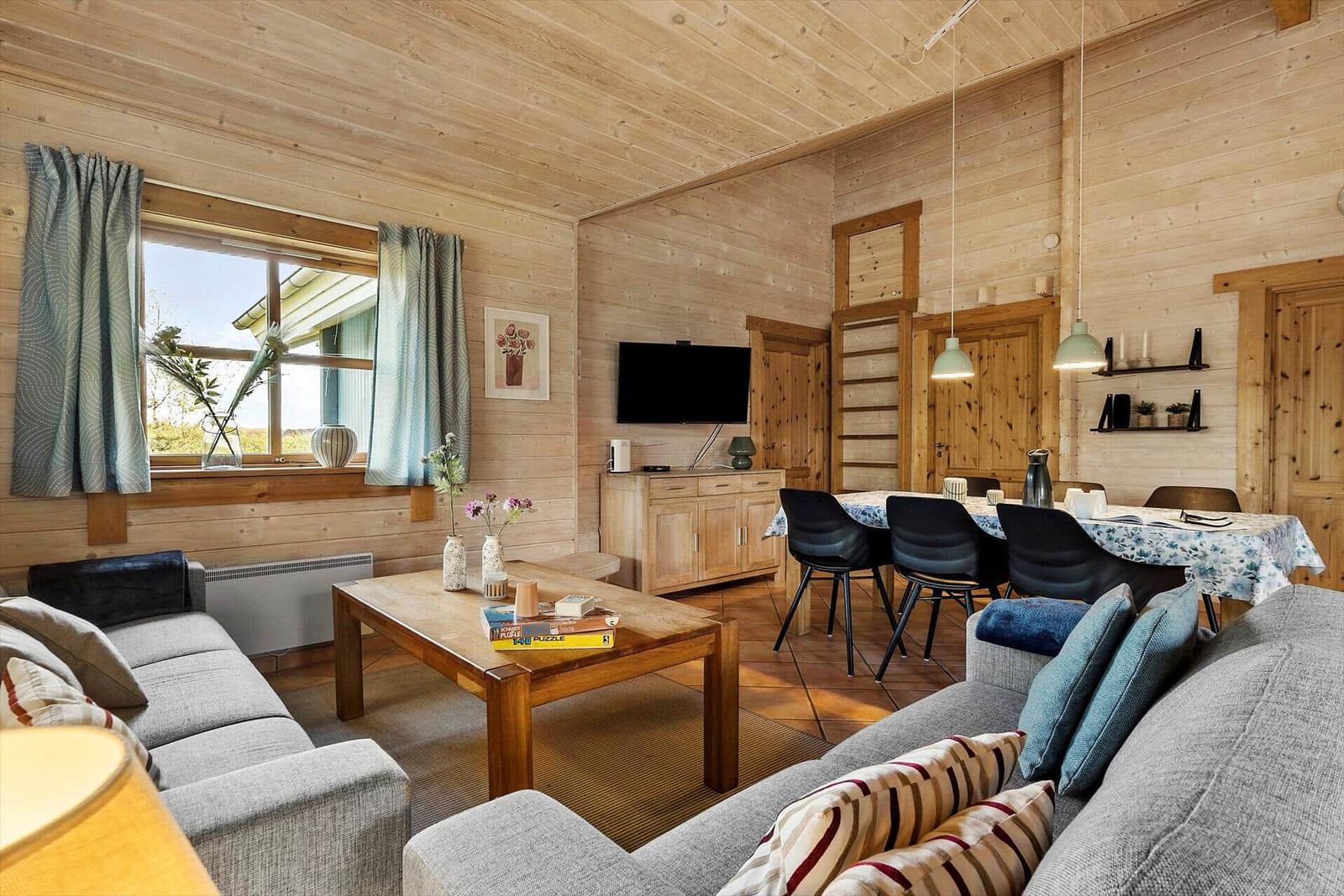 Wohn- und Essbereich mit Holzwand, Sofa, Tisch und Fernseher.