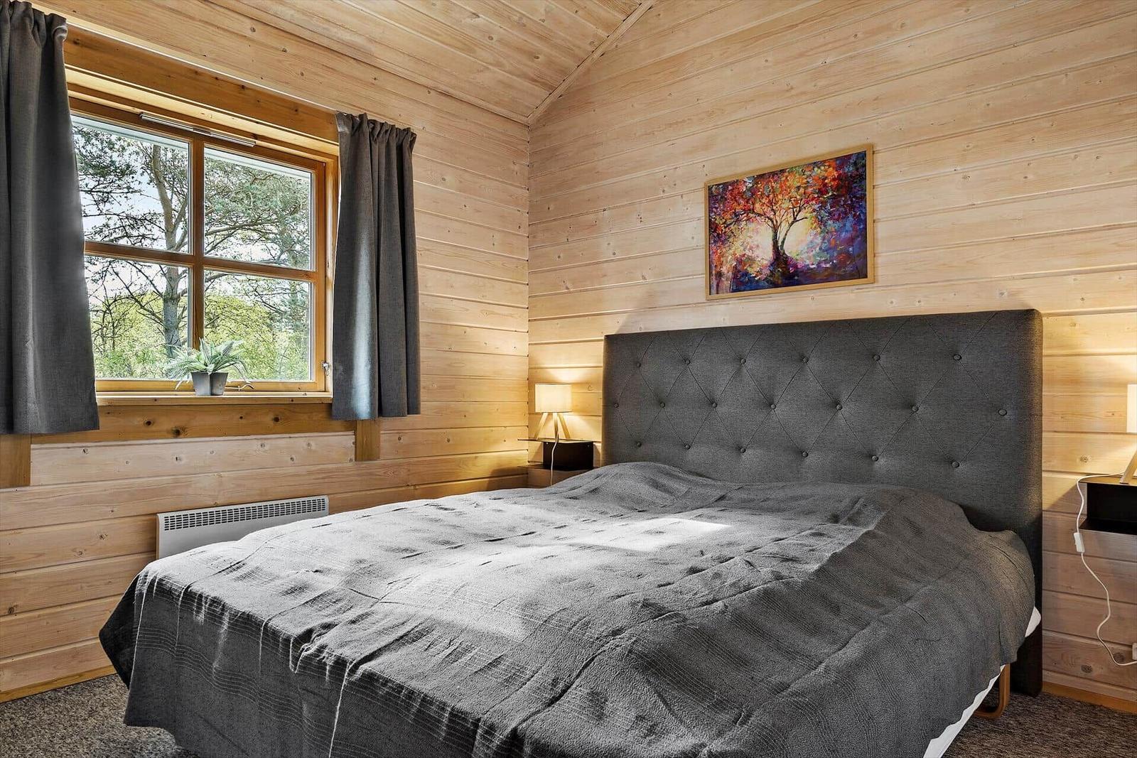Schlafzimmer mit Holzwand, Bett und Fenster mit Blick auf Bäume.