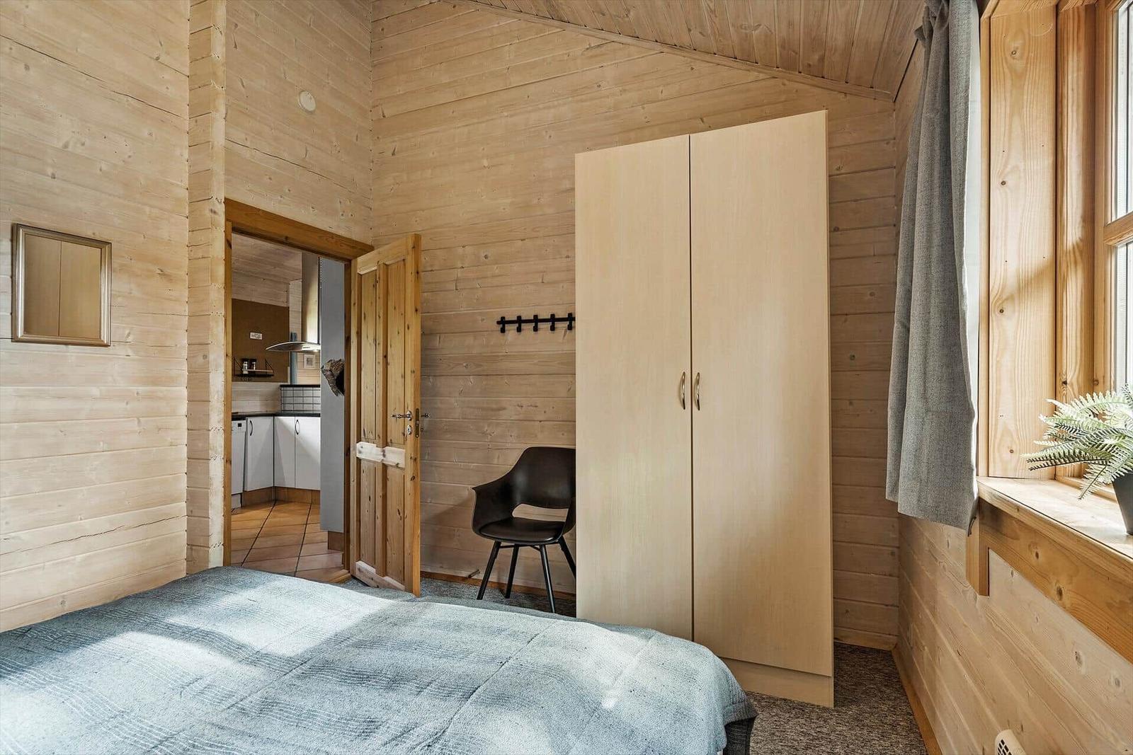 Schlafzimmer mit Holzwand, Bett, Kleiderschrank und Sicht auf Küche.