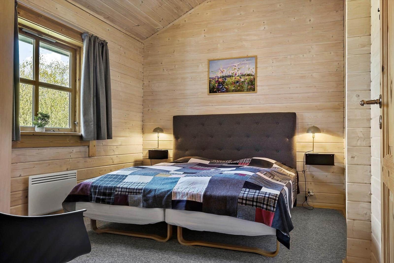 Schlafzimmer mit Holzwand, Bett, Fenster und Bild an der Wand.