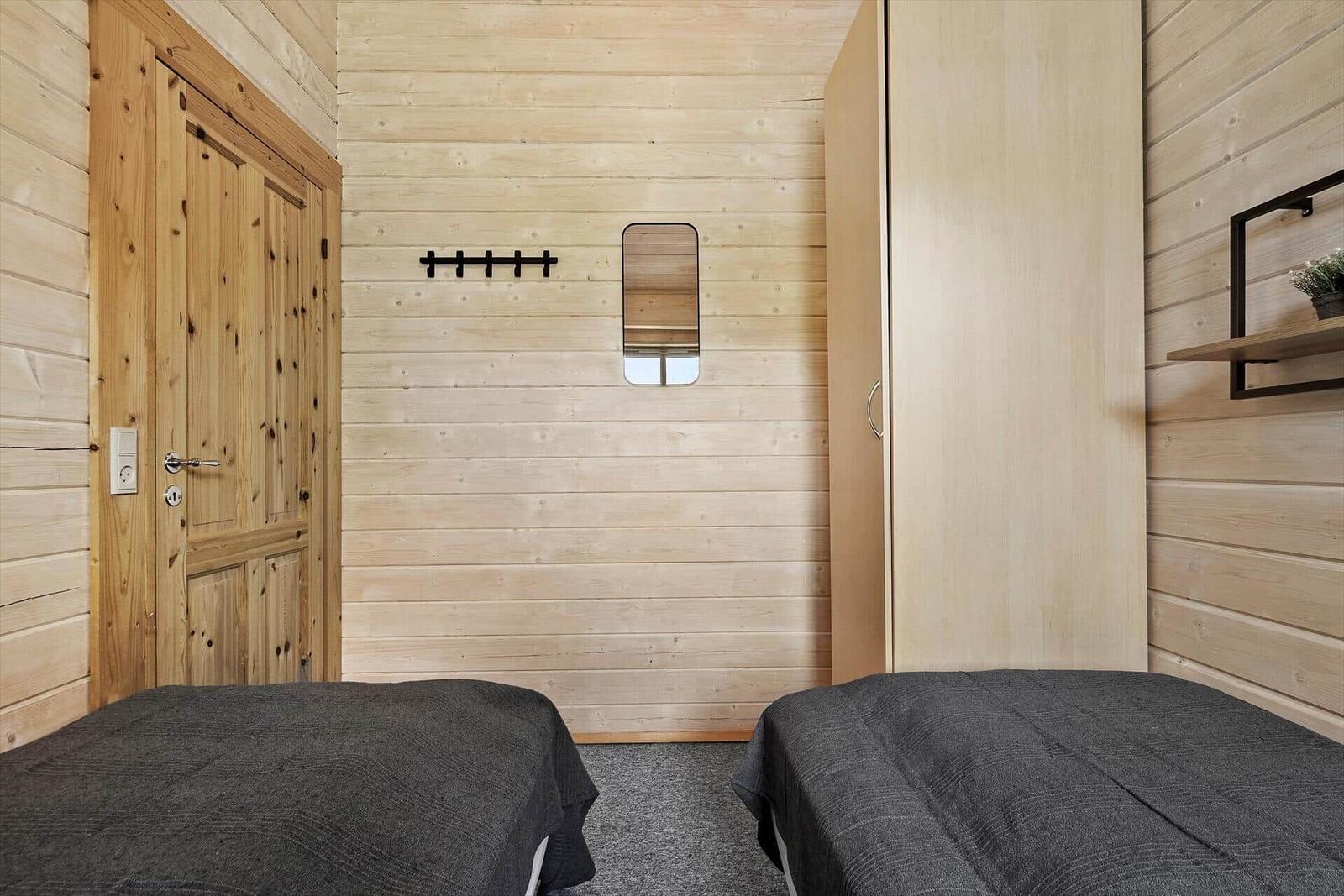 Zwei Betten, Holzwand, Kleiderkabine und Wandspiegel im Schlafzimmer.