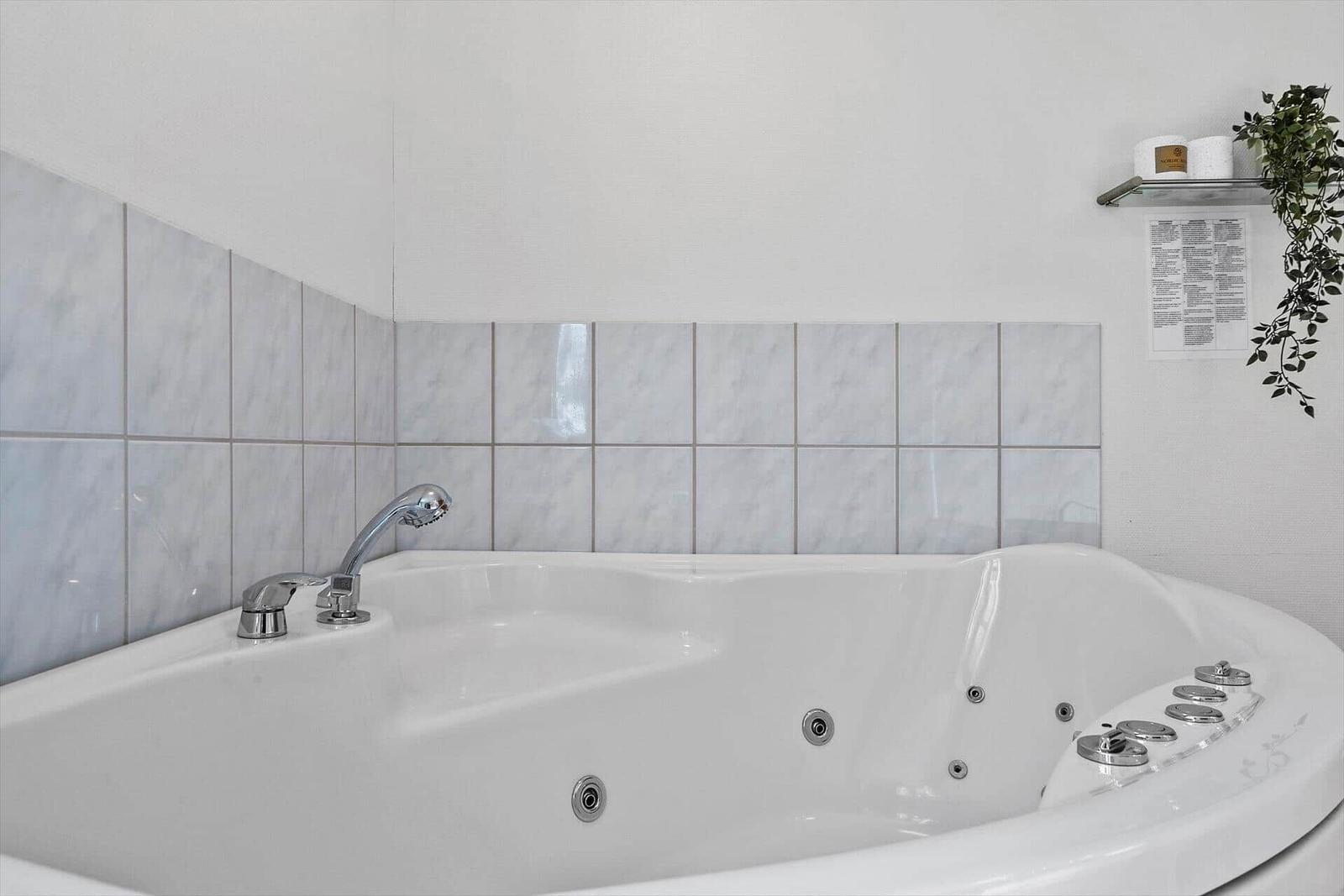 Eine Badewanne mit Duschkopf und Steuerungselementen. Wand mit hellen Fliesen.