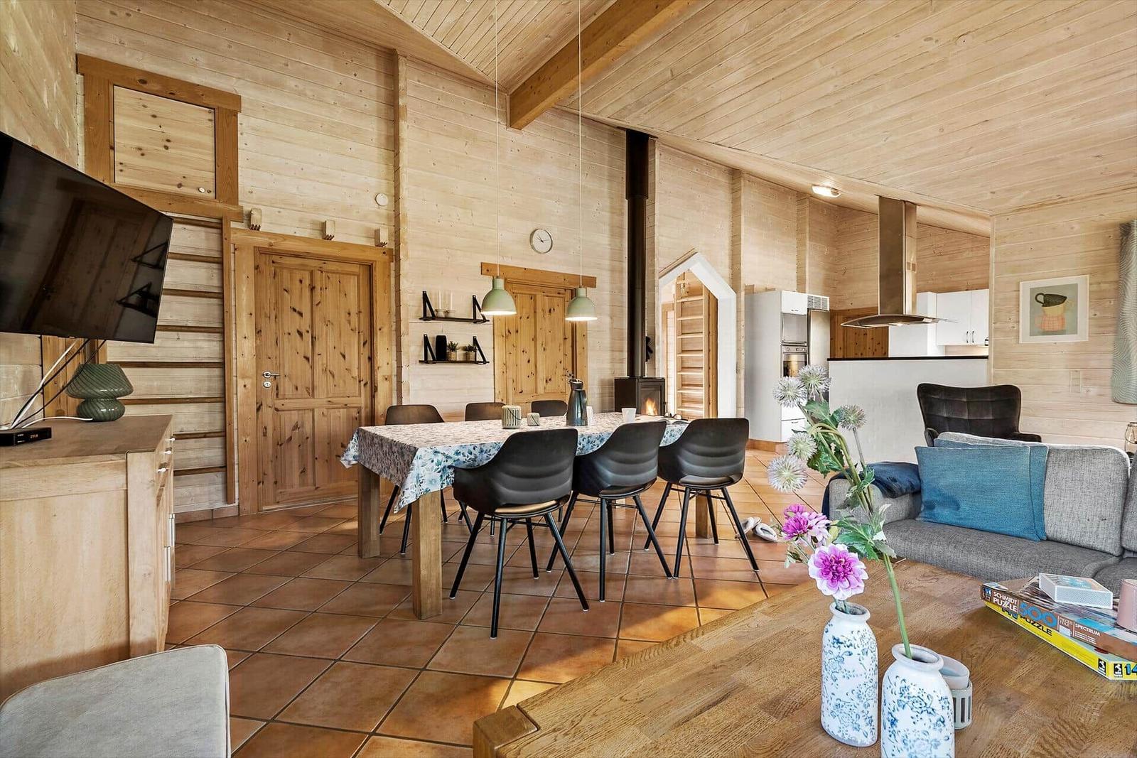 Wohn- und Essbereich mit Holzwand, Esstisch, Sofa und Kamin.