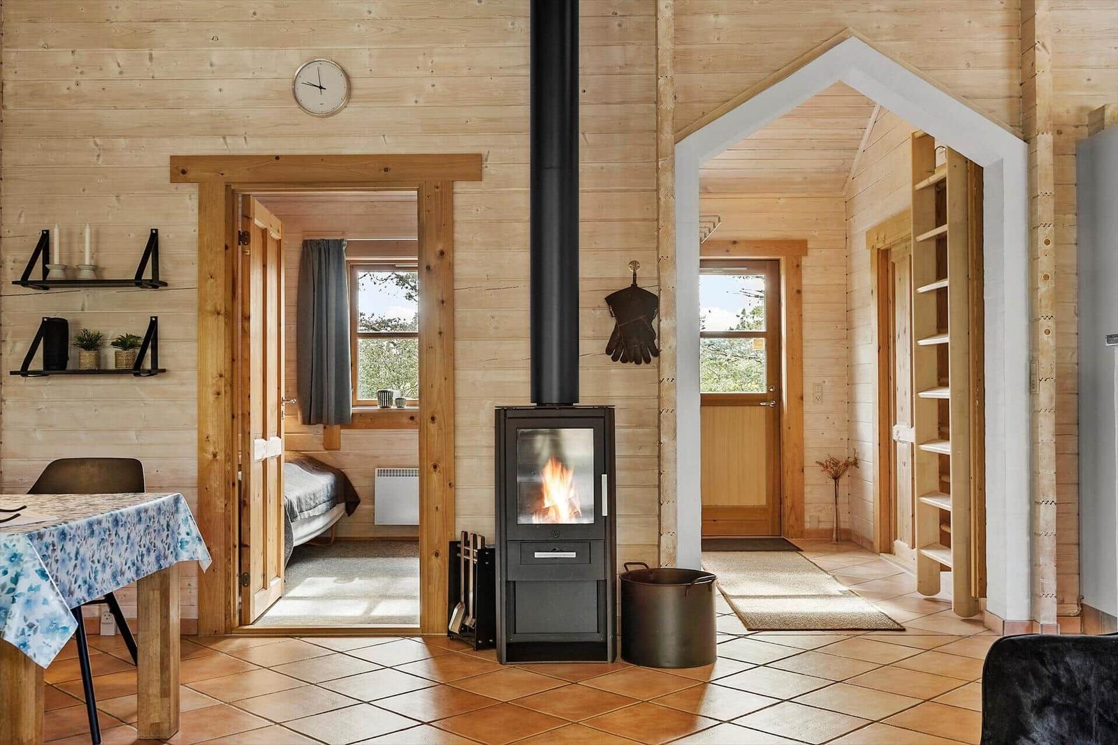 Wohnraum mit Holzwand, Kaminofen und Blick in Schlafzimmer und Flur.