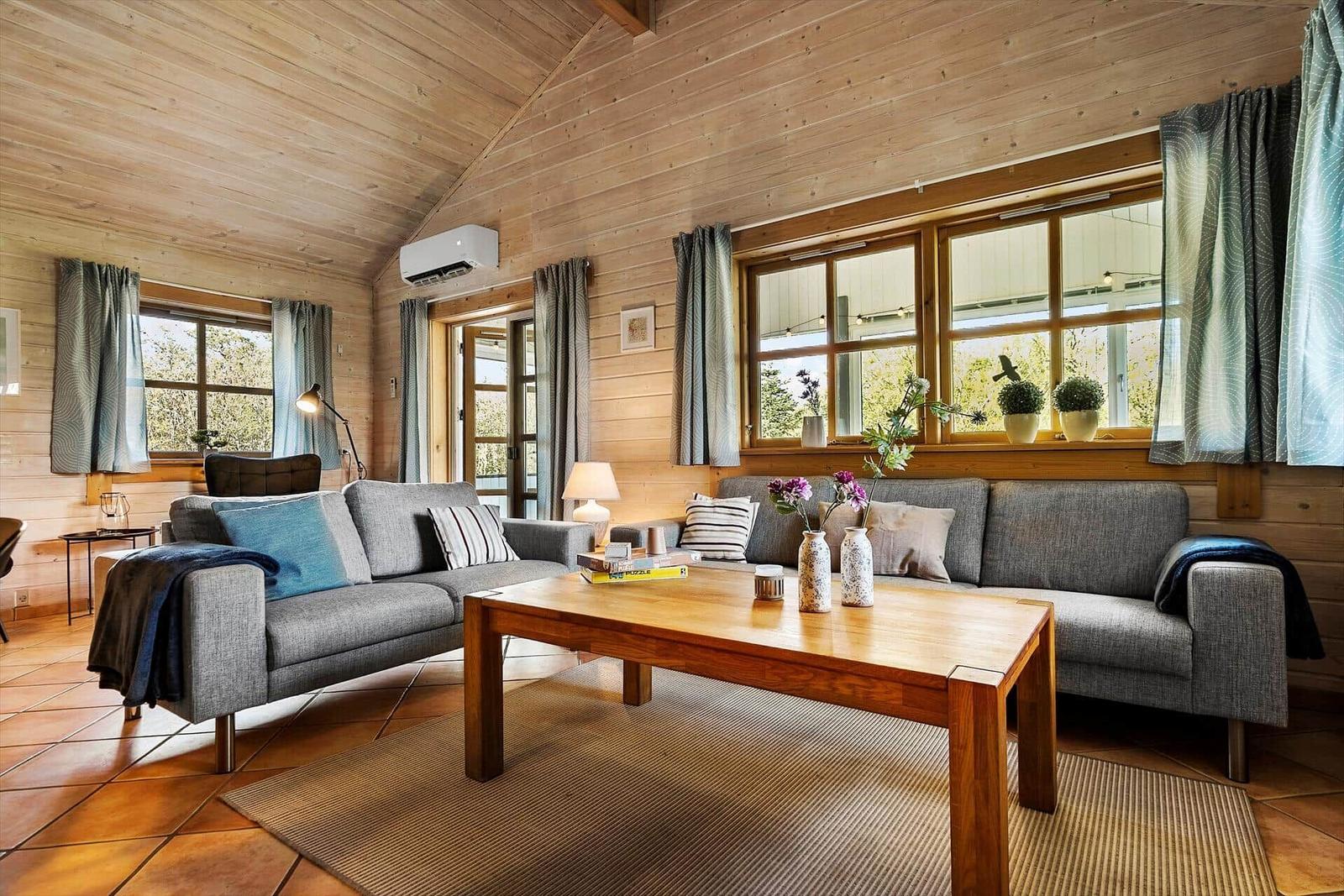 Wohnzimmer mit Holzwand, Sofa, Tisch und Fenstern.