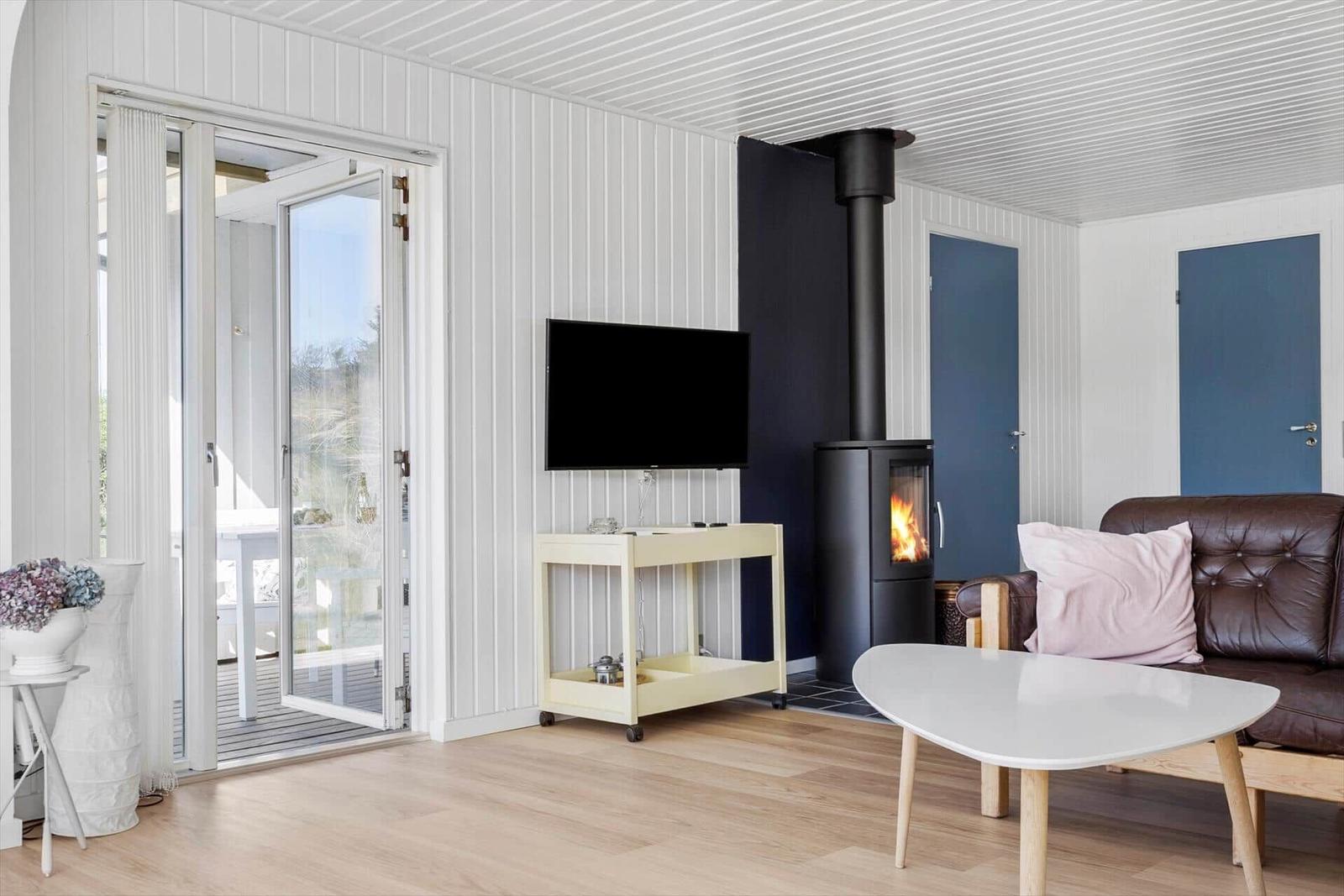 Wohnzimmer mit Kamin, TV und braunem Sofa. Glastür führt auf die Terrasse.
