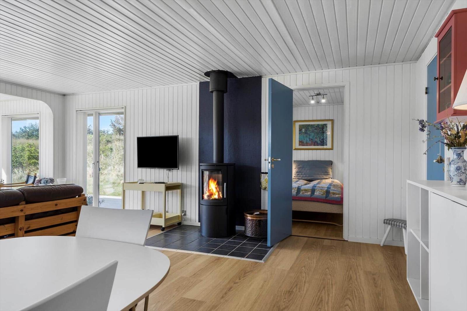 Wohnraum mit Kamin, Schlafzimmer und Essbereich. Holzfußboden und weiße Wände.