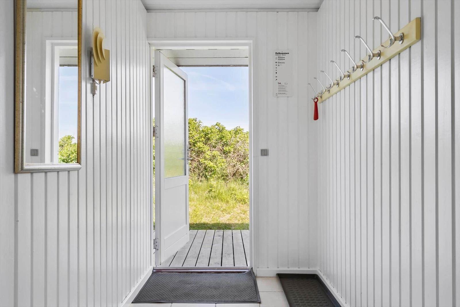 Eingangsbereich mit weißer Holzwand, Garderobe und Tür zum Außenbereich.
