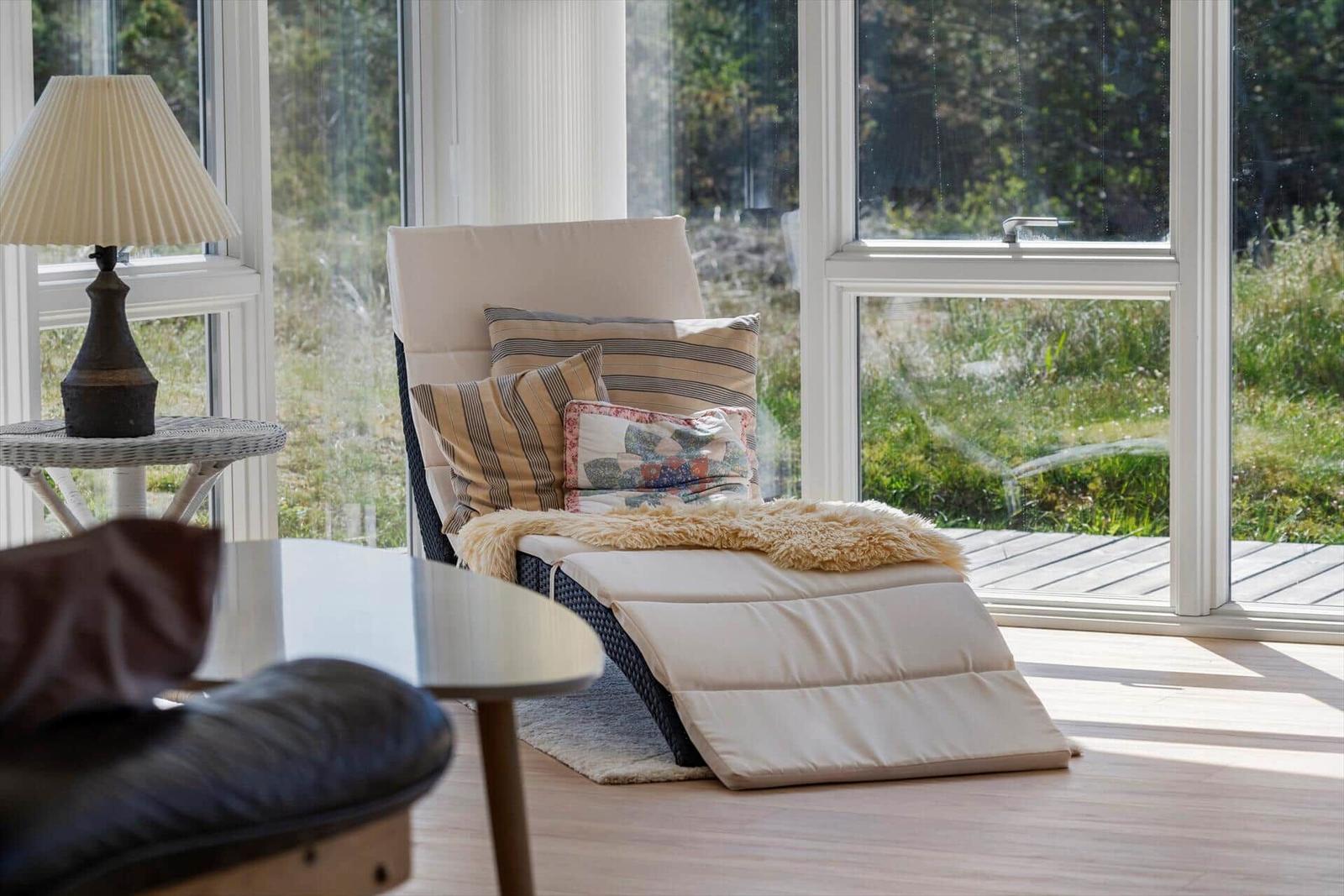 Liegende Couch mit Kissen und Felldecke vor großem Fenster mit Blick auf Grünfläche.