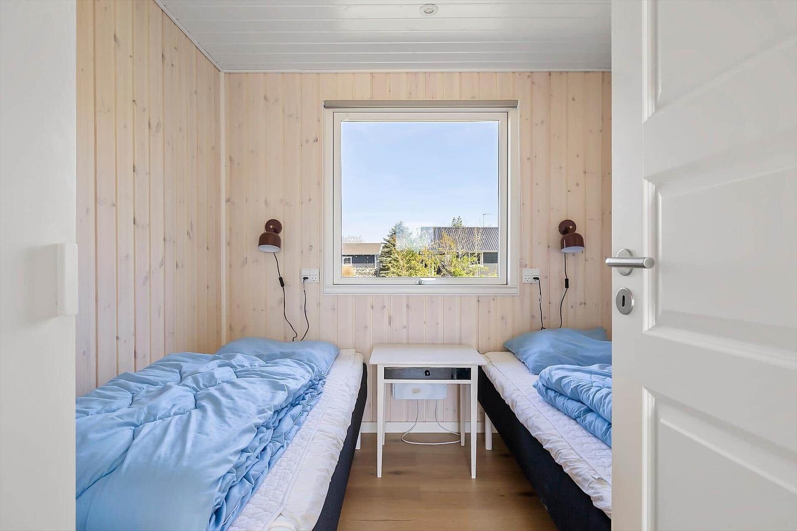 Zwei Betten mit blauen Decken, Holzwände, Fenster und Nachttisch.