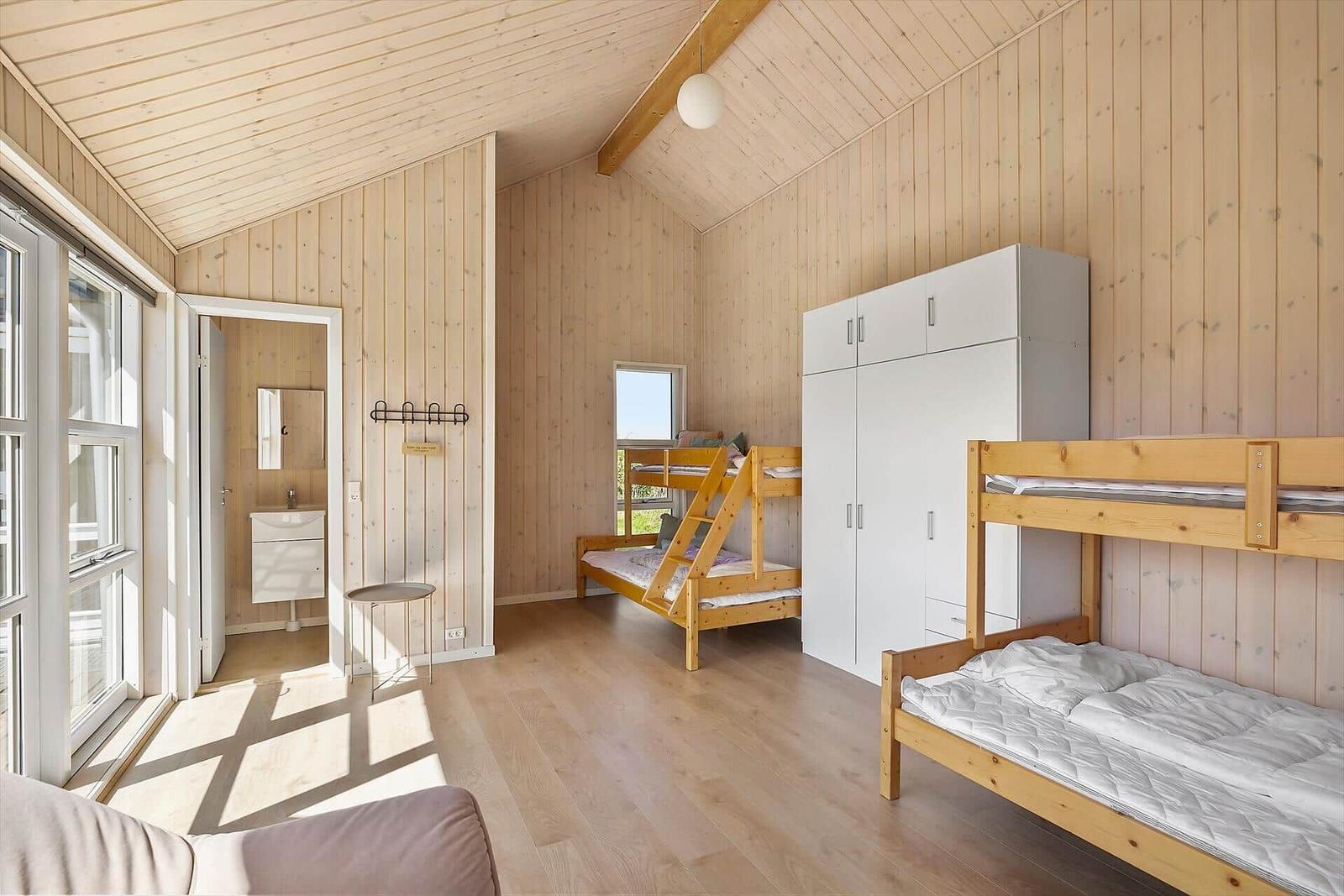 Zimmer mit zwei Etagenbetten, weißem Schrank und Holzwandverkleidung. Dusche und Fenster sind sichtbar.