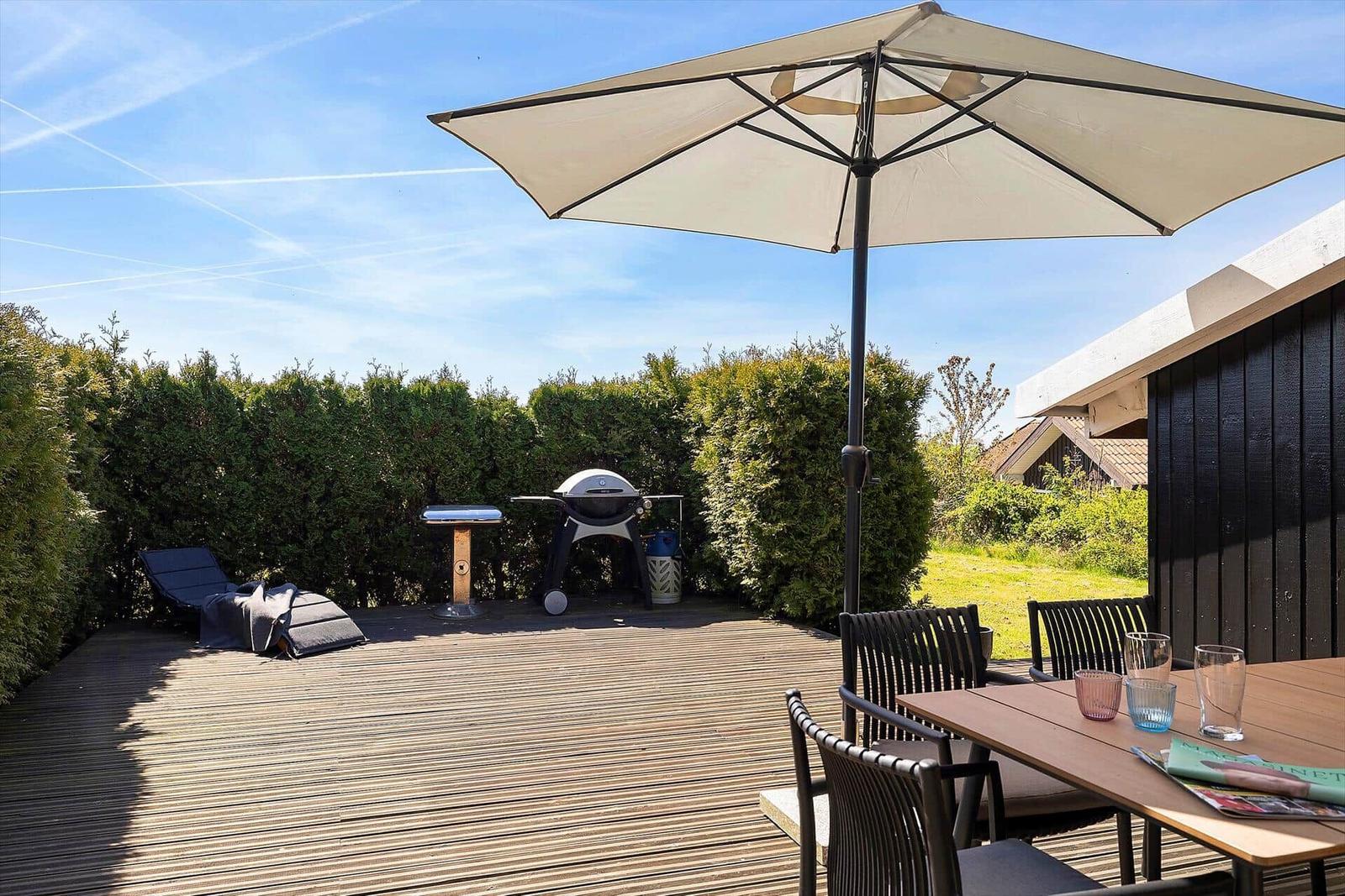 Terrasse mit Sonnenschirm, Grill und Esstisch mit Stühlen.