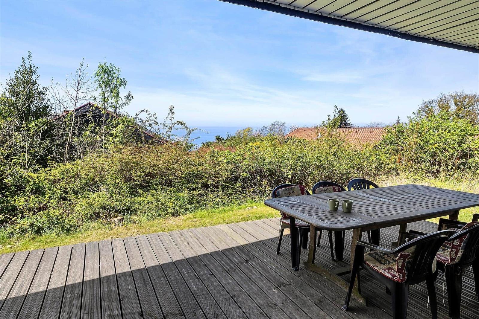 Terrasse mit Tisch und Stühlen, Blick auf Wald und Meer.