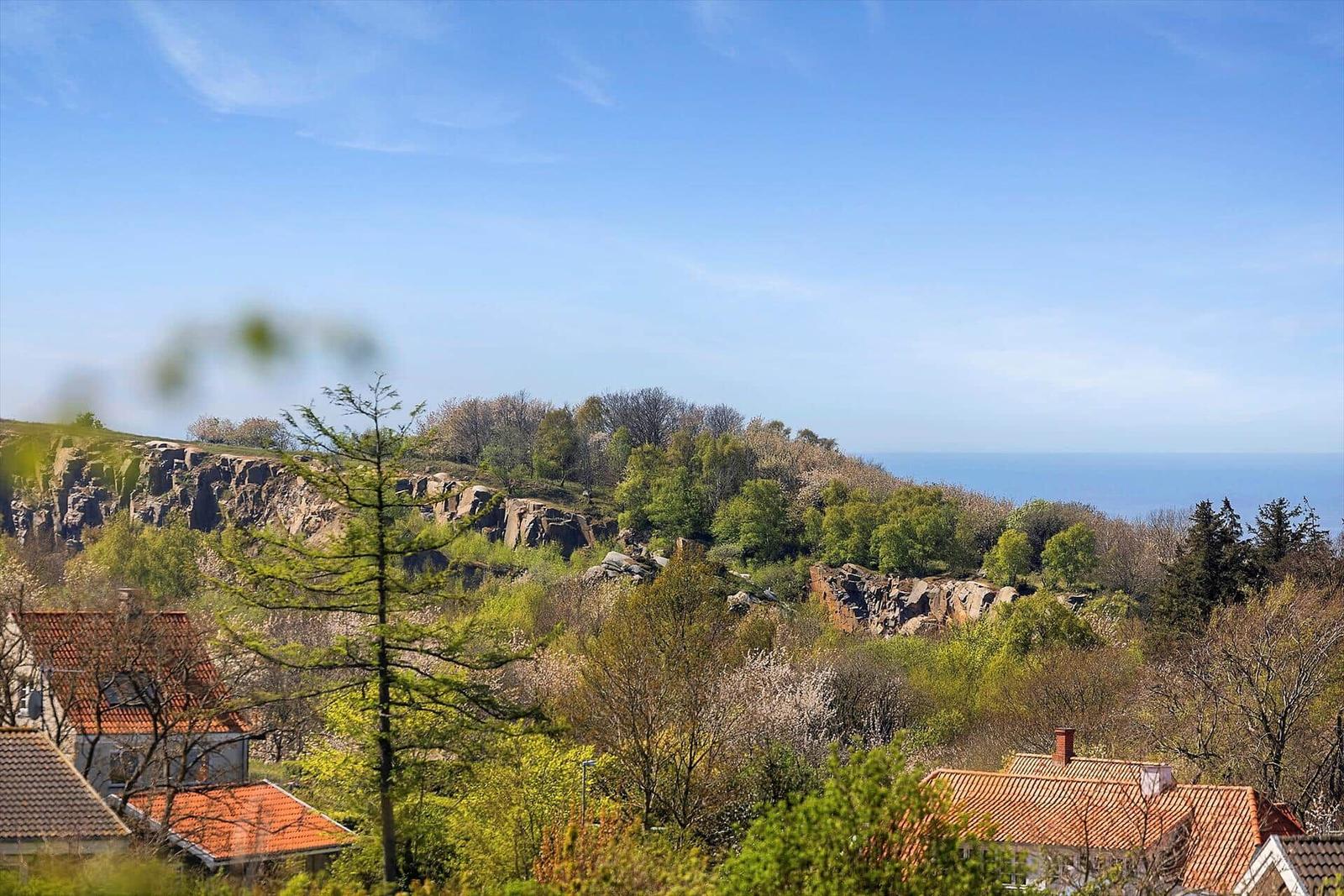 Haus mit rotem Dach, Blick auf Hügel und Meer unter blauem Himmel.