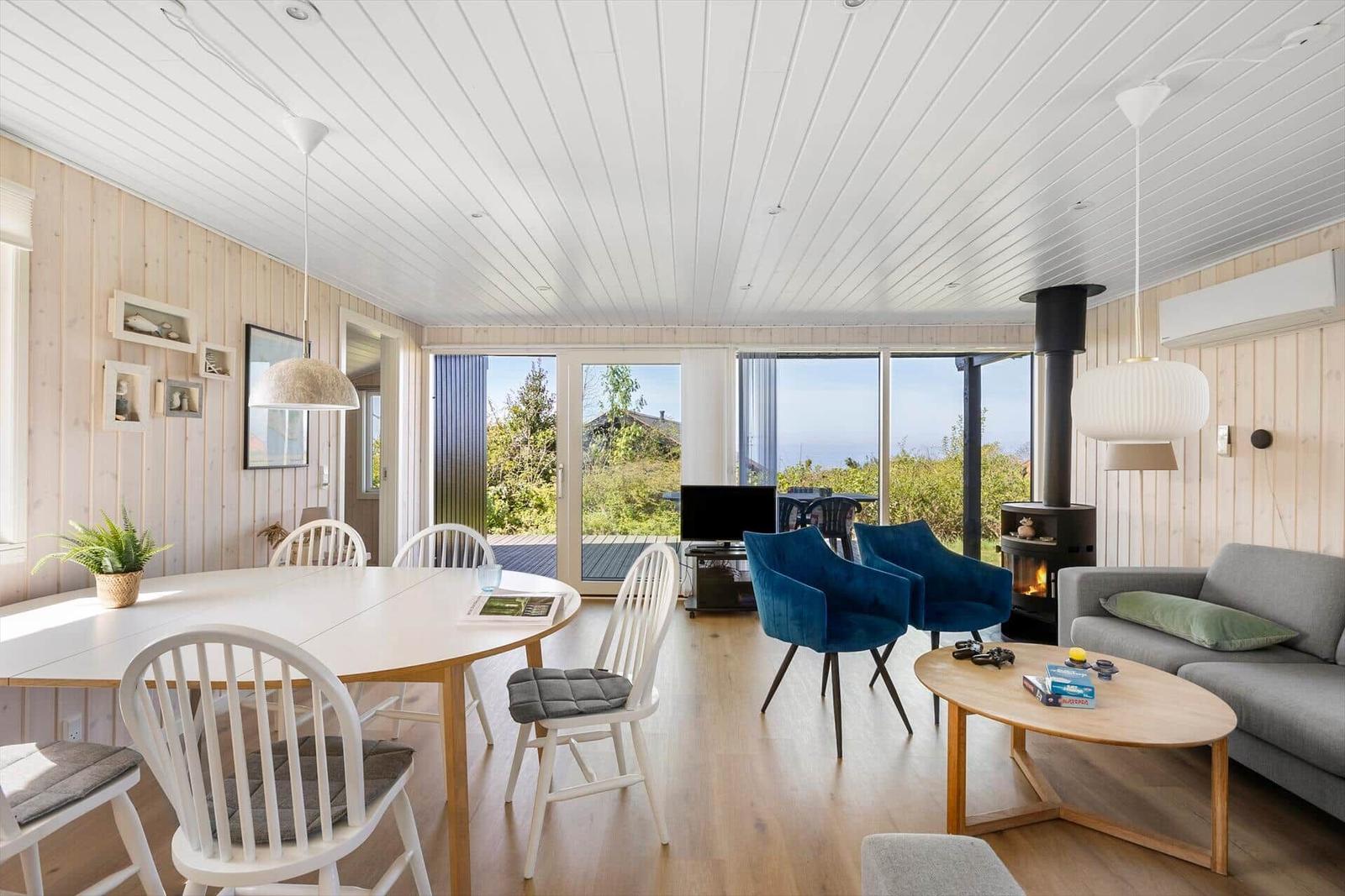 Wohn- und Essbereich mit Holzwänden, großen Fenstern und einem Kamin.