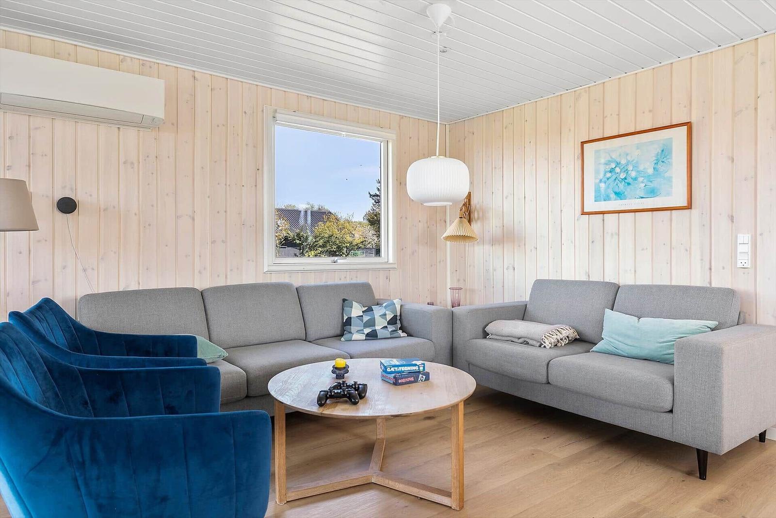 Wohnzimmer mit grauem Sofa, blauem Sessel und runden Tisch.