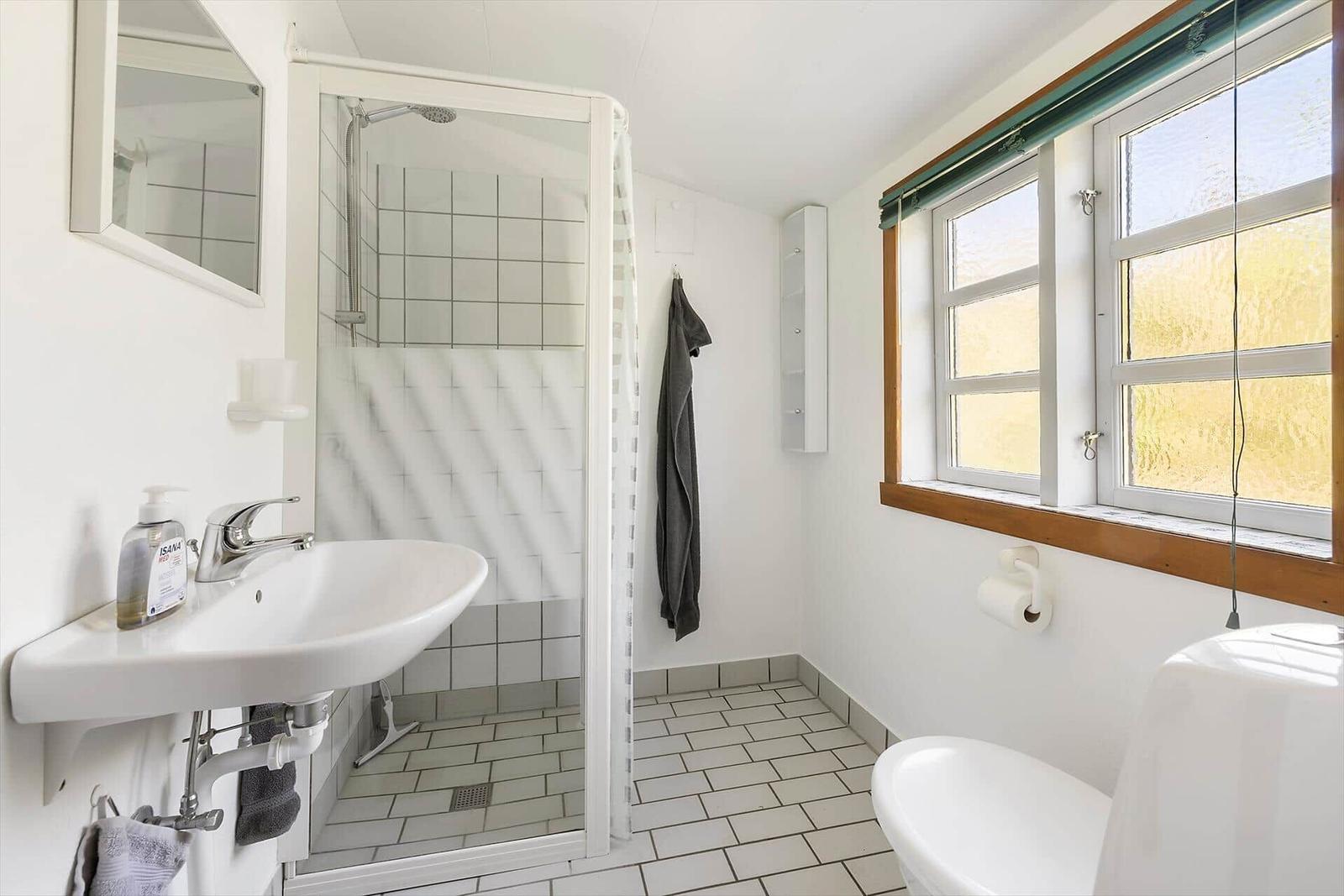 Badezimmer mit Dusche, Waschbecken und Toilette. Fenster mit Holzrahmen.