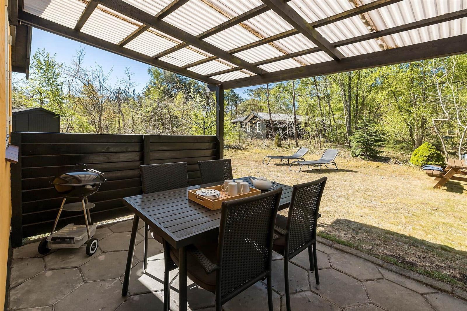 Terrasse mit Tisch, Stühlen, Grill und Blick in den Wald.