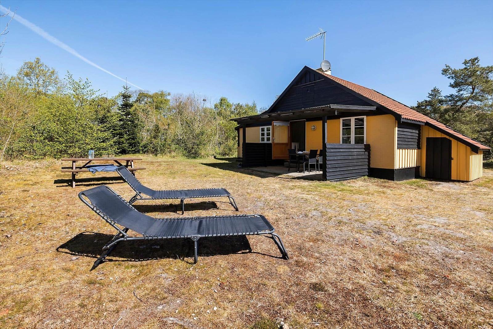 Haus mit Terrasse, Liegestühlen und Picknicktisch im Grünen.