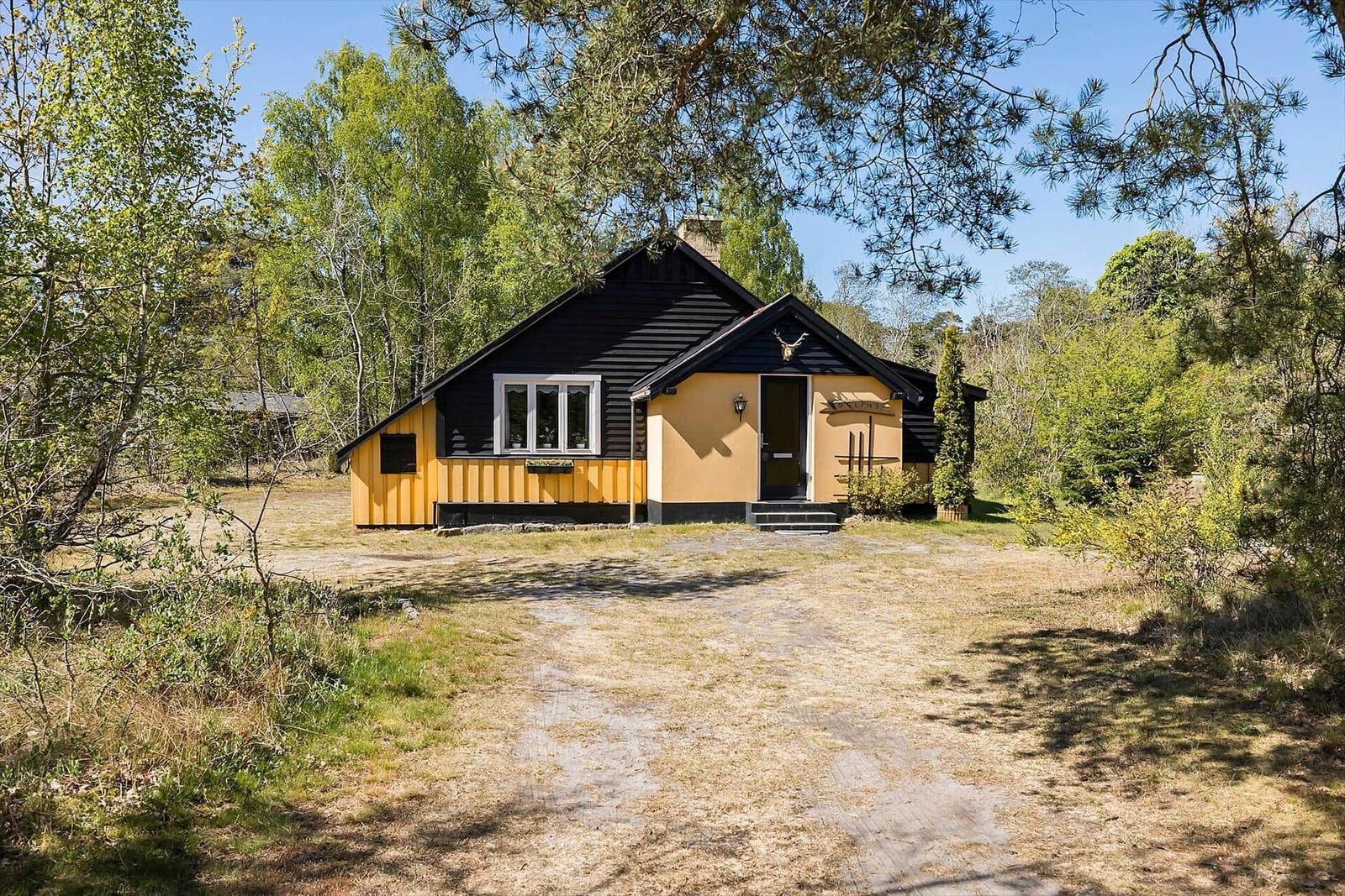 Ein gelbes Haus mit schwarzem Dach steht im Wald. Der Eingang ist mit Stufen versehen.