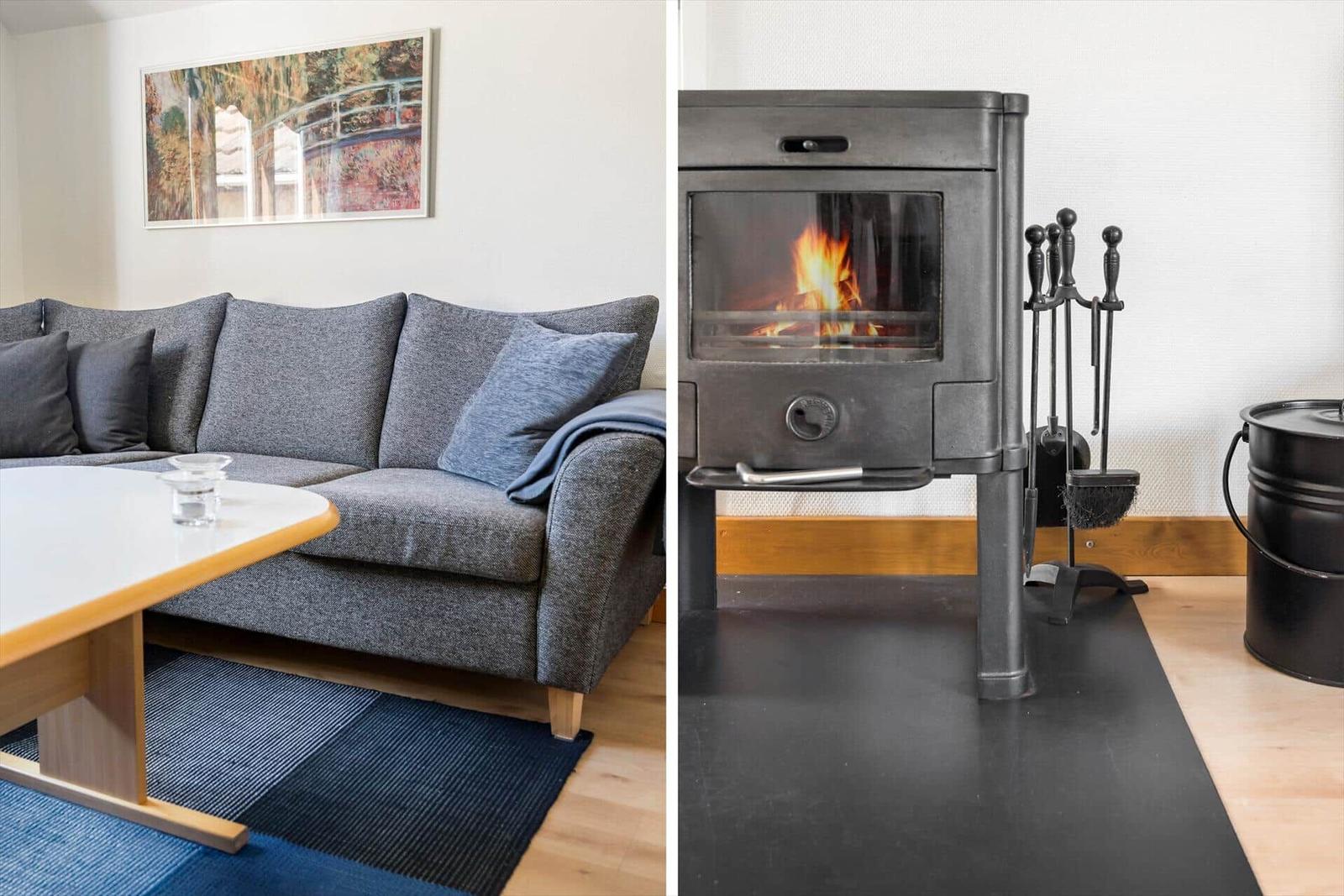 Grauer Sofa mit Kissen und Tisch. Holzofen mit Feuer und Werkzeug.