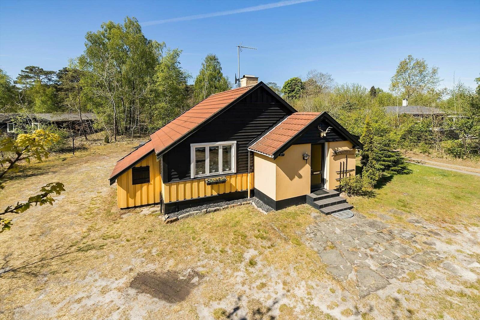 Holzhaus mit rotem Dach, gelben und schwarzen Wänden, Eingangstreppe und Garten.