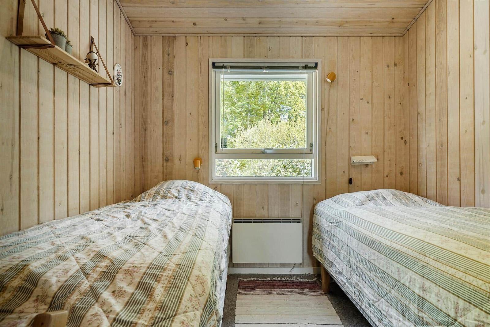 Zwei Betten in einem Zimmer mit Holzwänden und einem Fenster mit Blick auf Bäume.