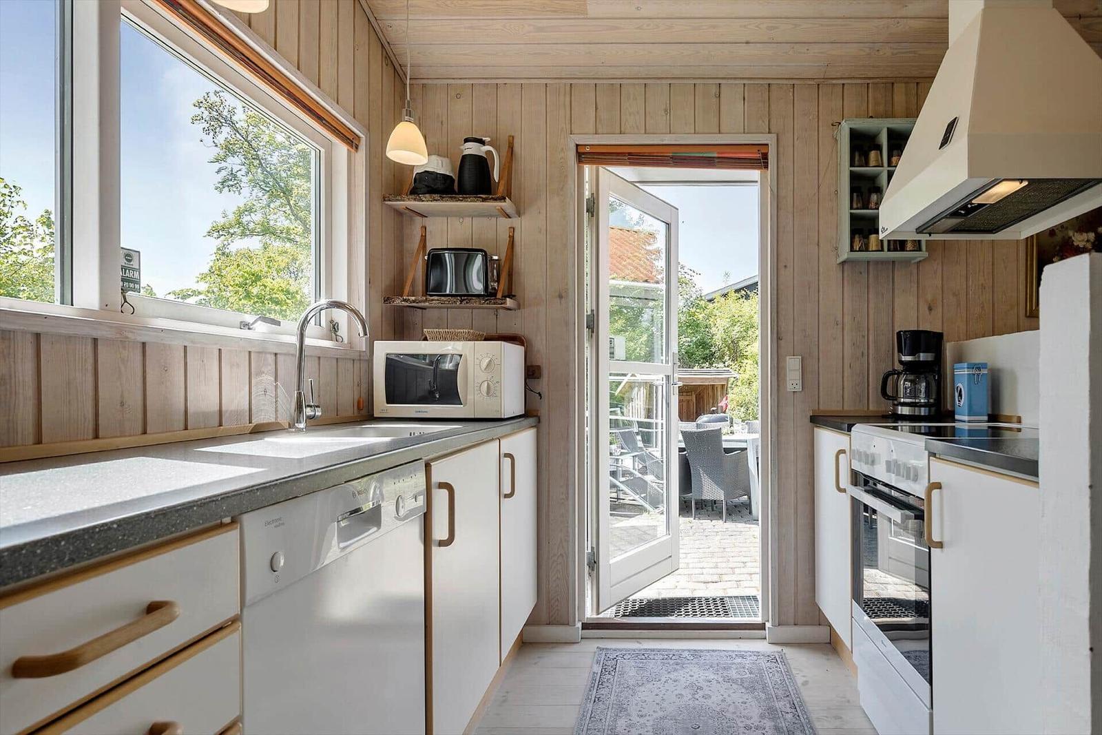 Küche mit Fenster, Tür zum Balkon und weißen Schränken.