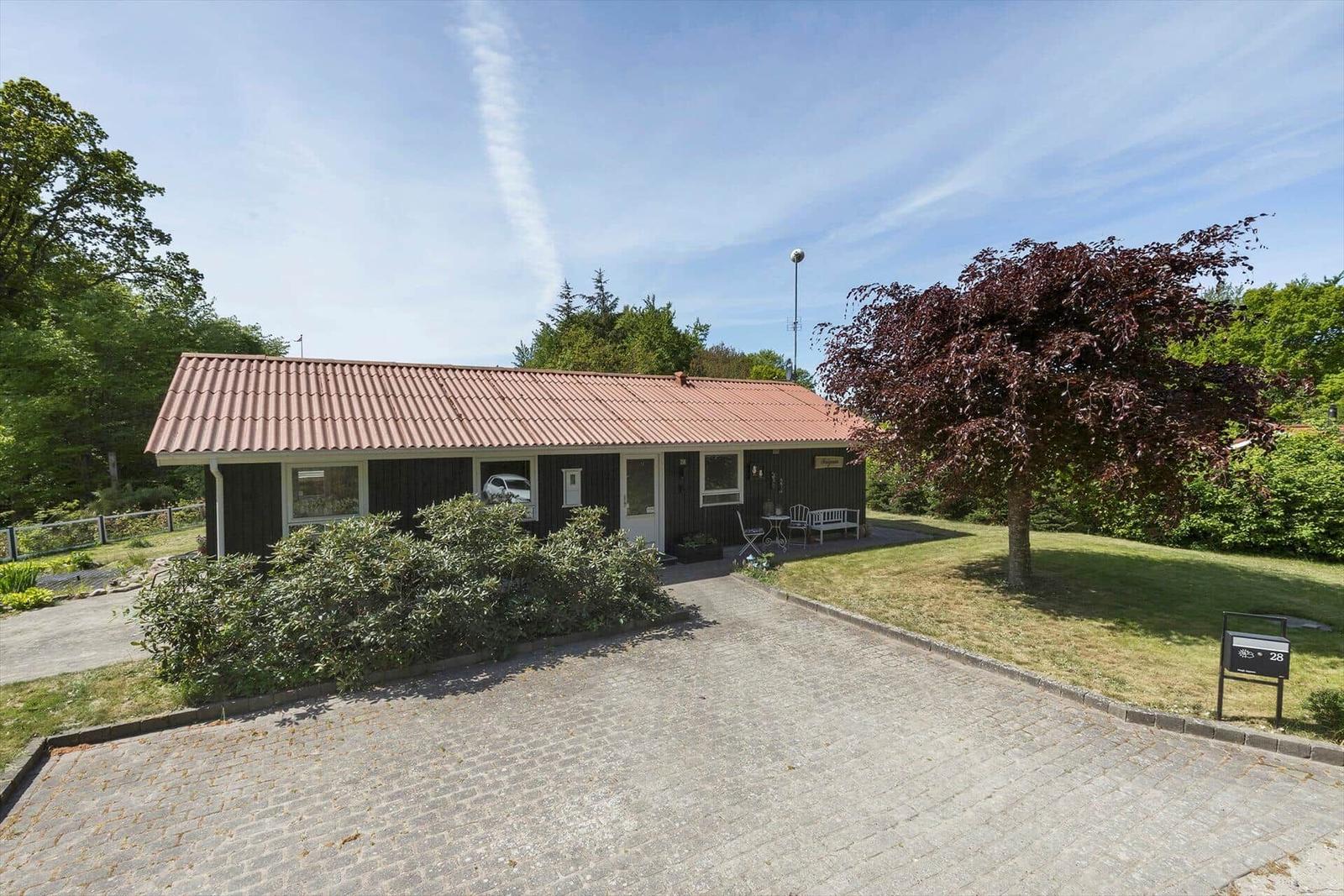 Einhaus mit Terrasse, Garten und gepflastertem Weg. Ein Baum mit roten Blättern steht daneben.