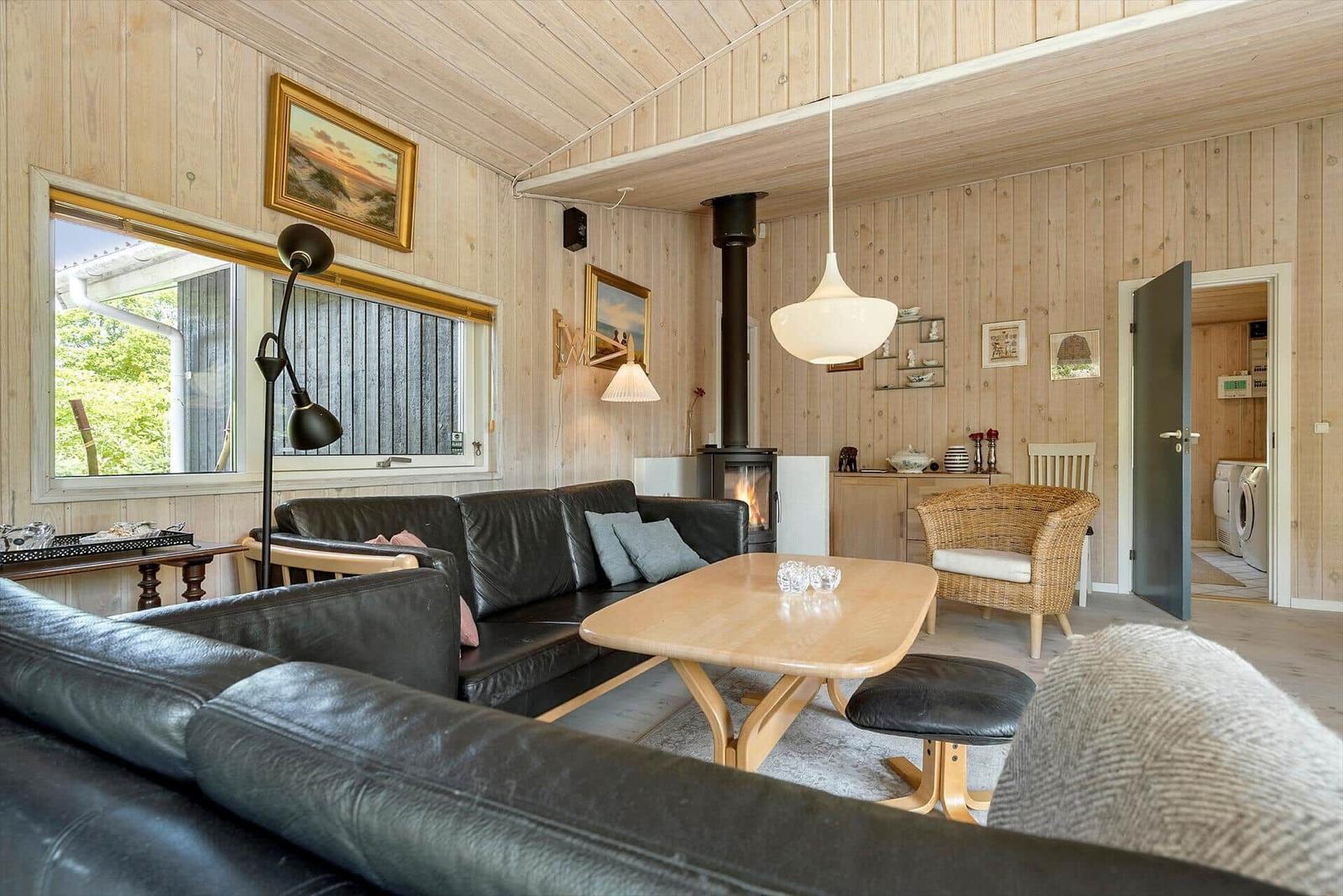 Wohnzimmer mit Holzwand, Sofa, Tisch und Kaminofen. Durchgang zur Küche.